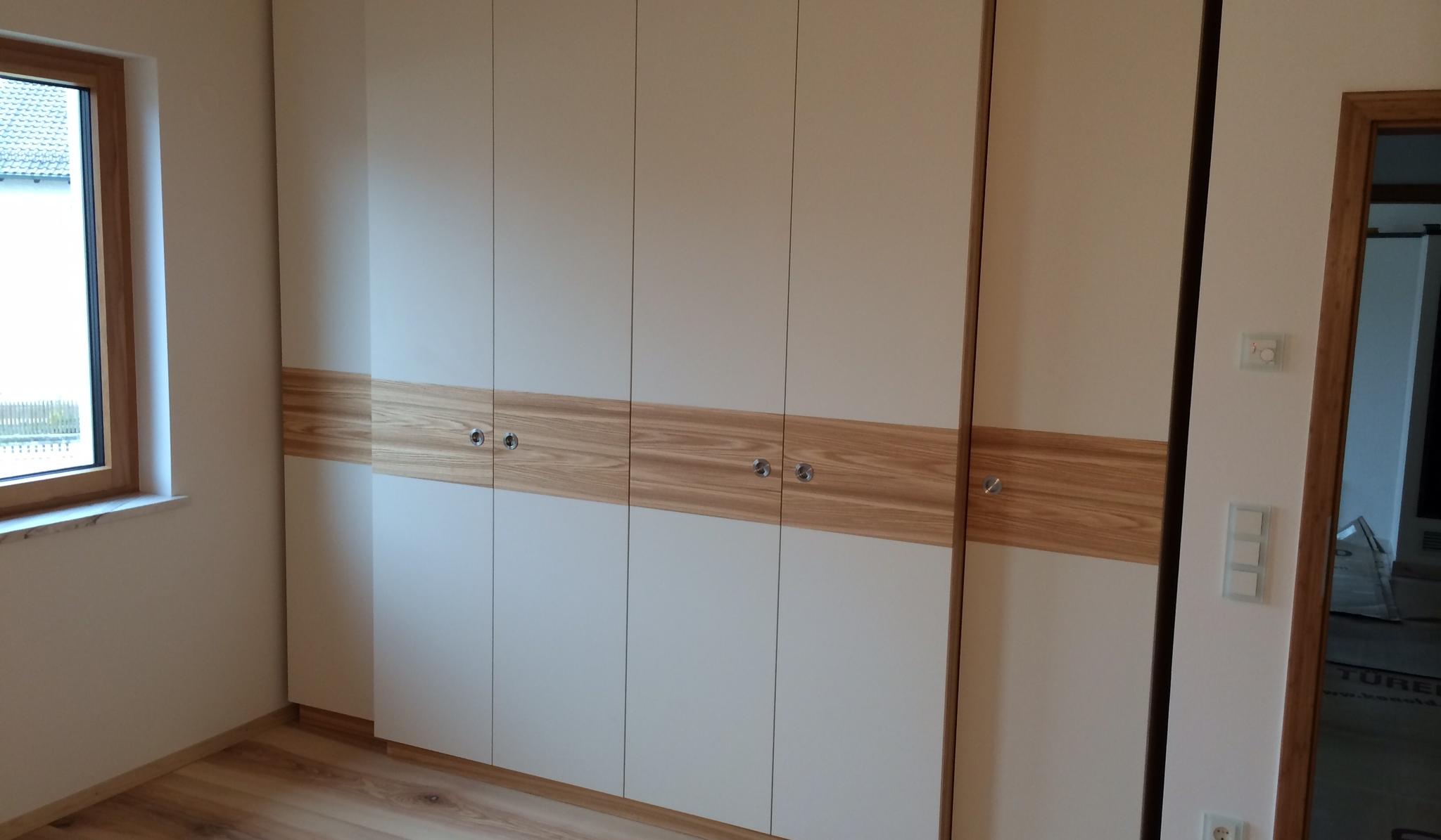 Großer weißer Einbauschrank mit Holzdekor in einem hellen Zimmer.