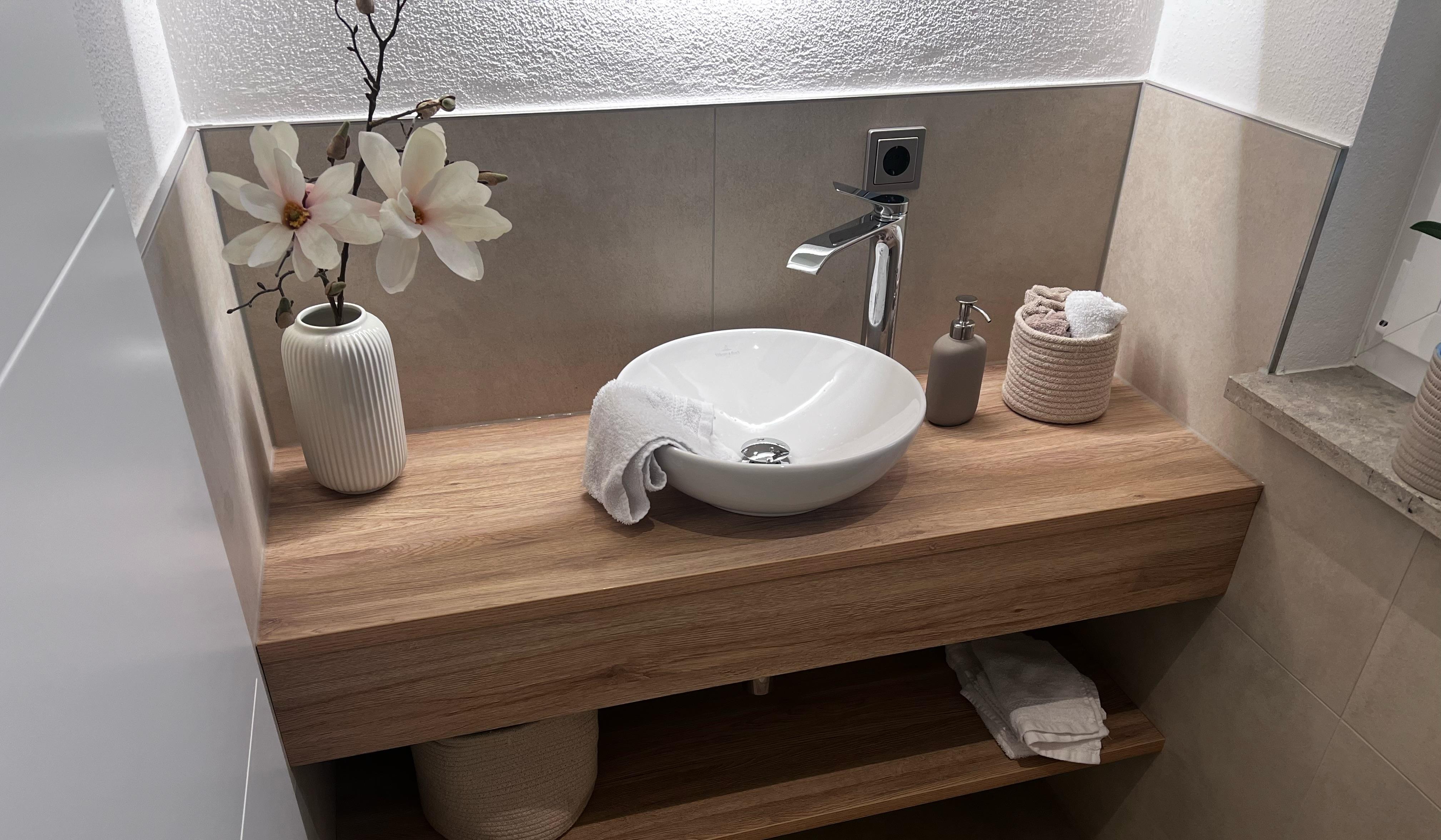 Modernes Waschbecken auf Holzplatte, Vase mit Blumen, Handtuch und Seifenspender.