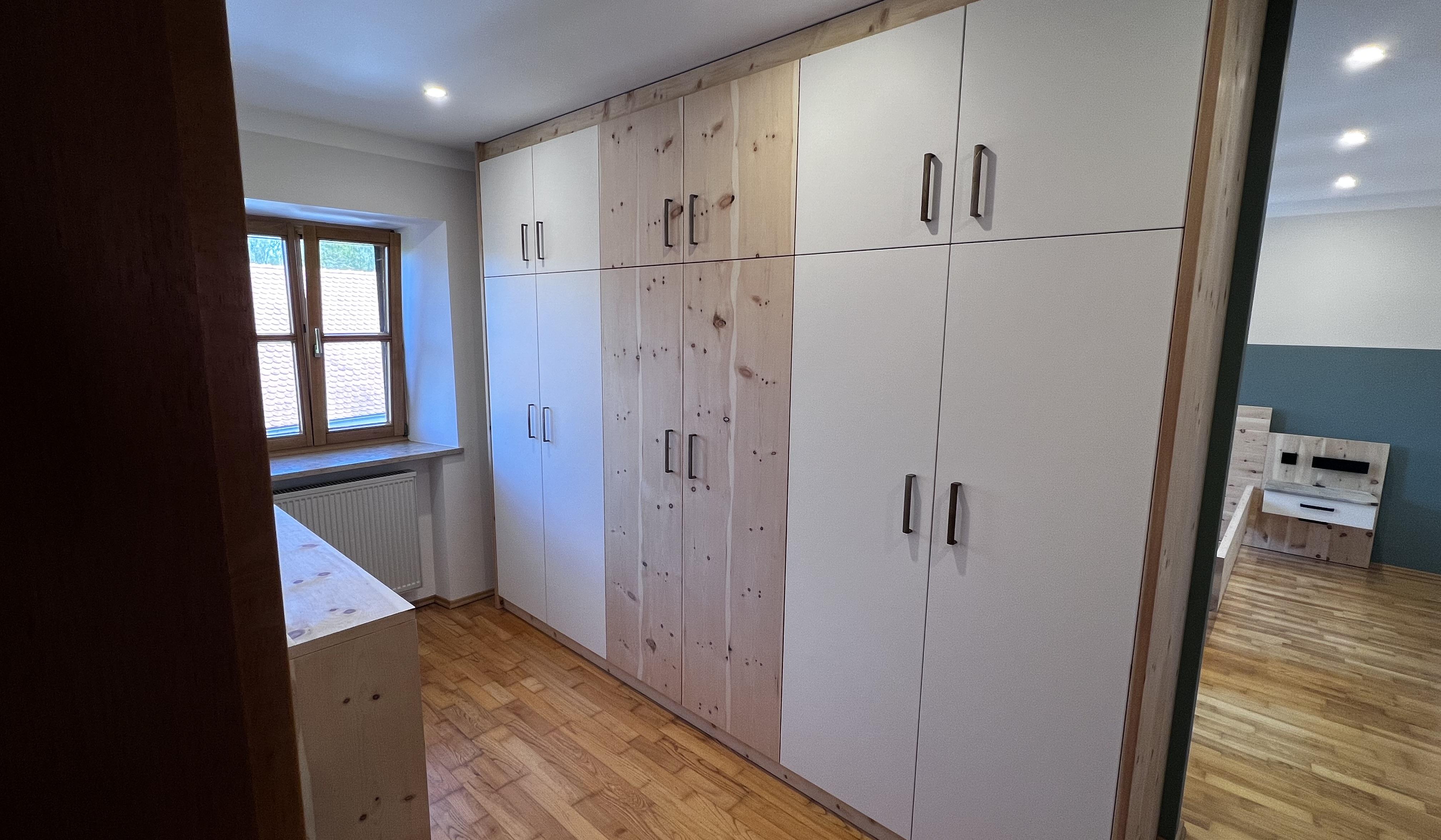 Heller Raum mit großem Einbauschrank aus Holz, Parkettboden und Fenster.