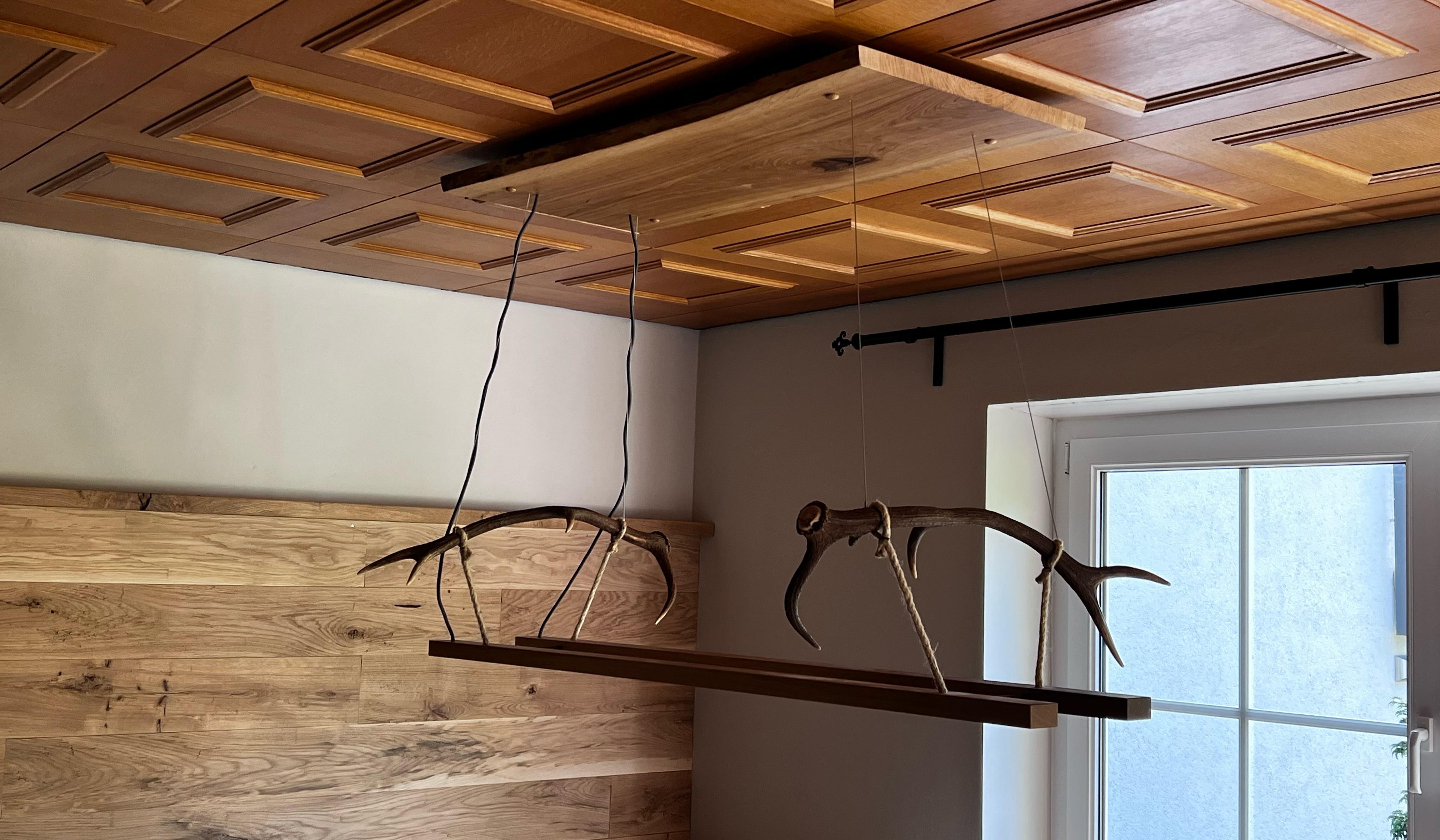 Holzlampe mit Rehfiguren hängt an einer Holzdecke in einem gemütlichen Zimmer.