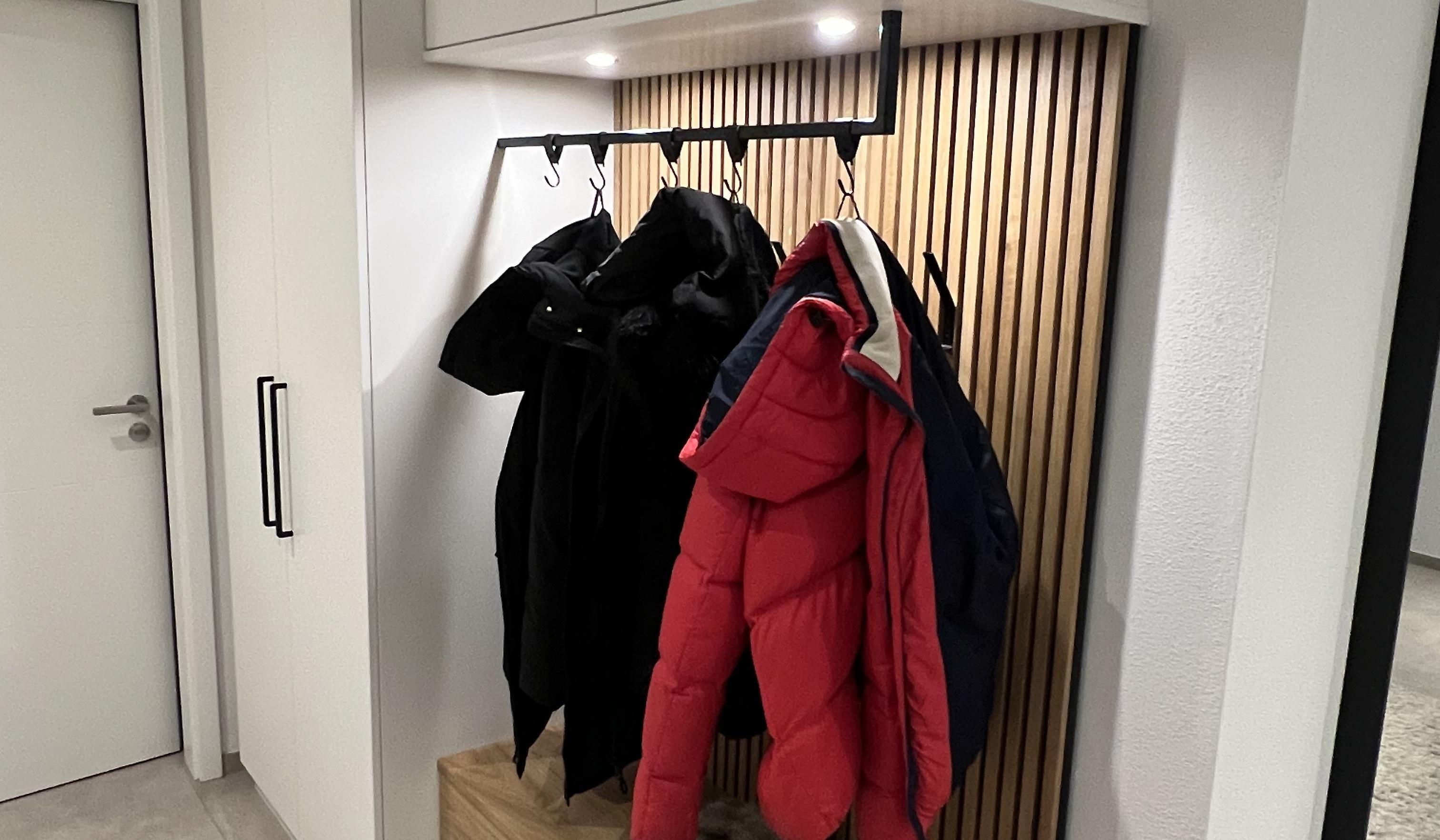 Garderobe mit Jacken, Holzbänken und weißen Schränken in modernem Flur.
