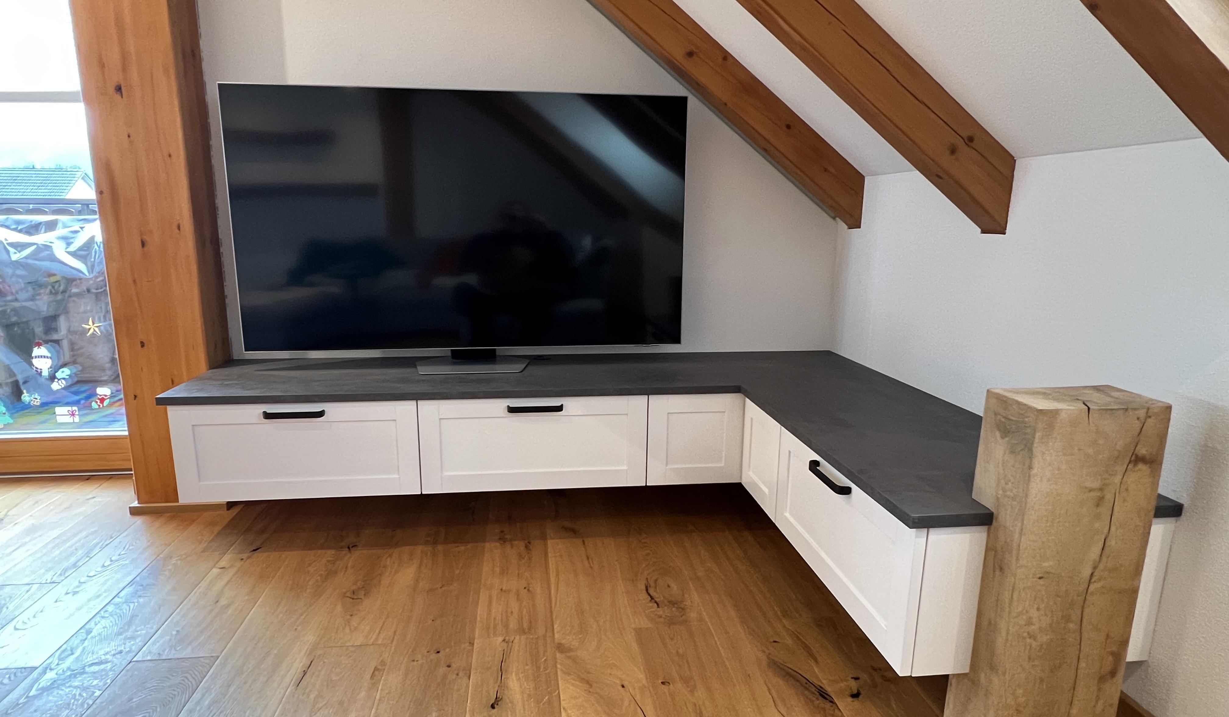 Flachbildfernseher auf weißem Eck-TV-Schrank mit Schubladen, Holzbalken und Parkettboden.