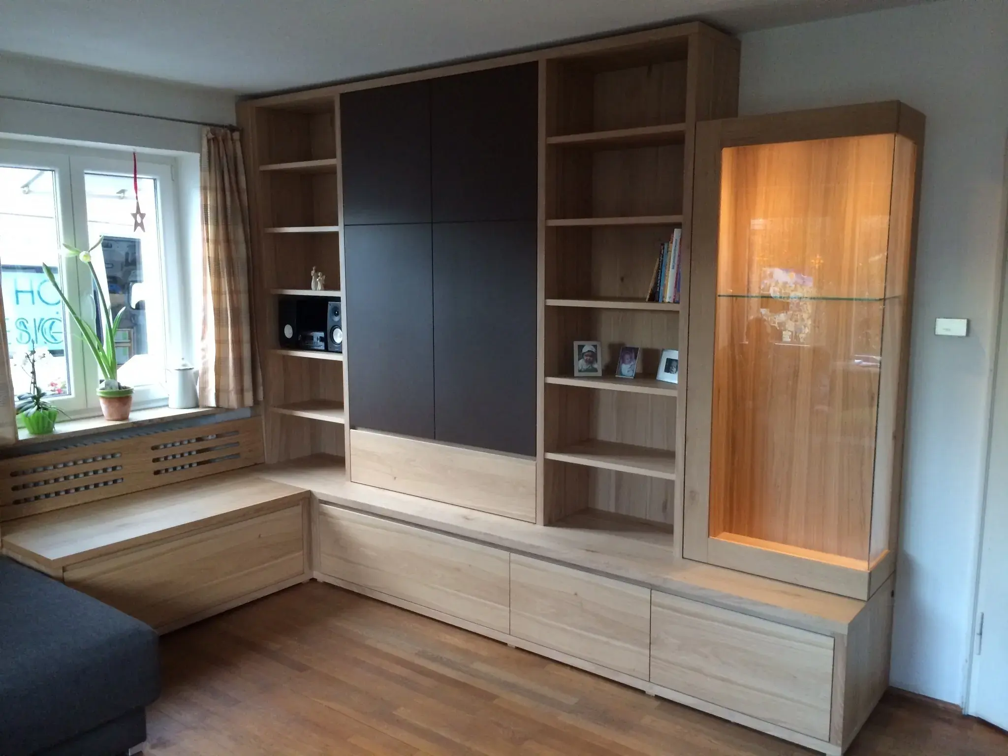 Modernes Wohnzimmerregal aus Holz mit Vitrine, Regalen und Sitzbank am Fenster.