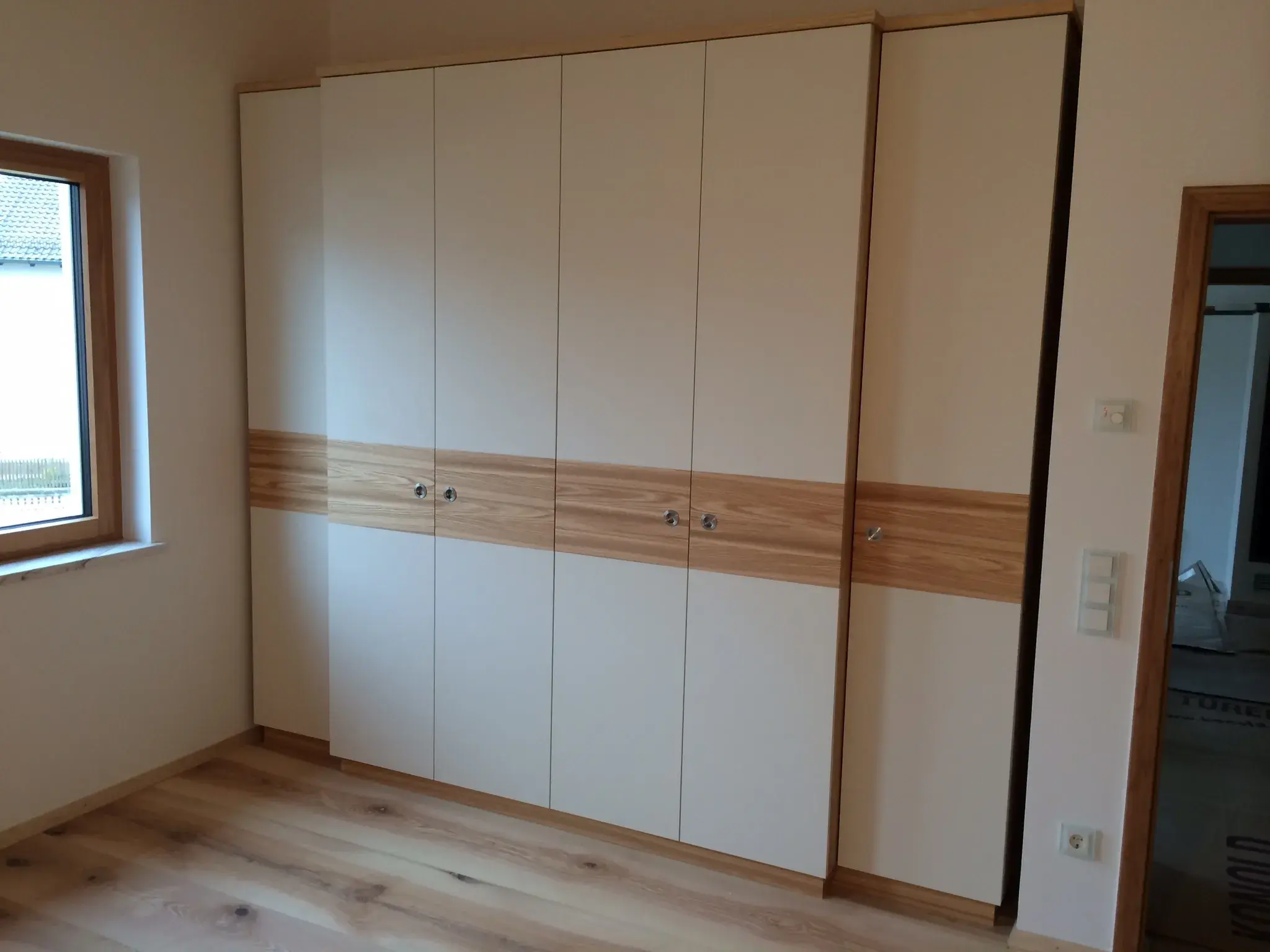 Großer weißer Einbauschrank mit Holzdekor in einem hellen Zimmer.