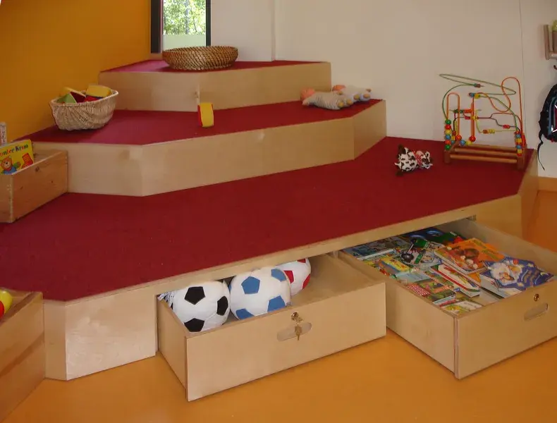 Spielfläche mit rotem Teppich zum Klettern und mit Stauraum