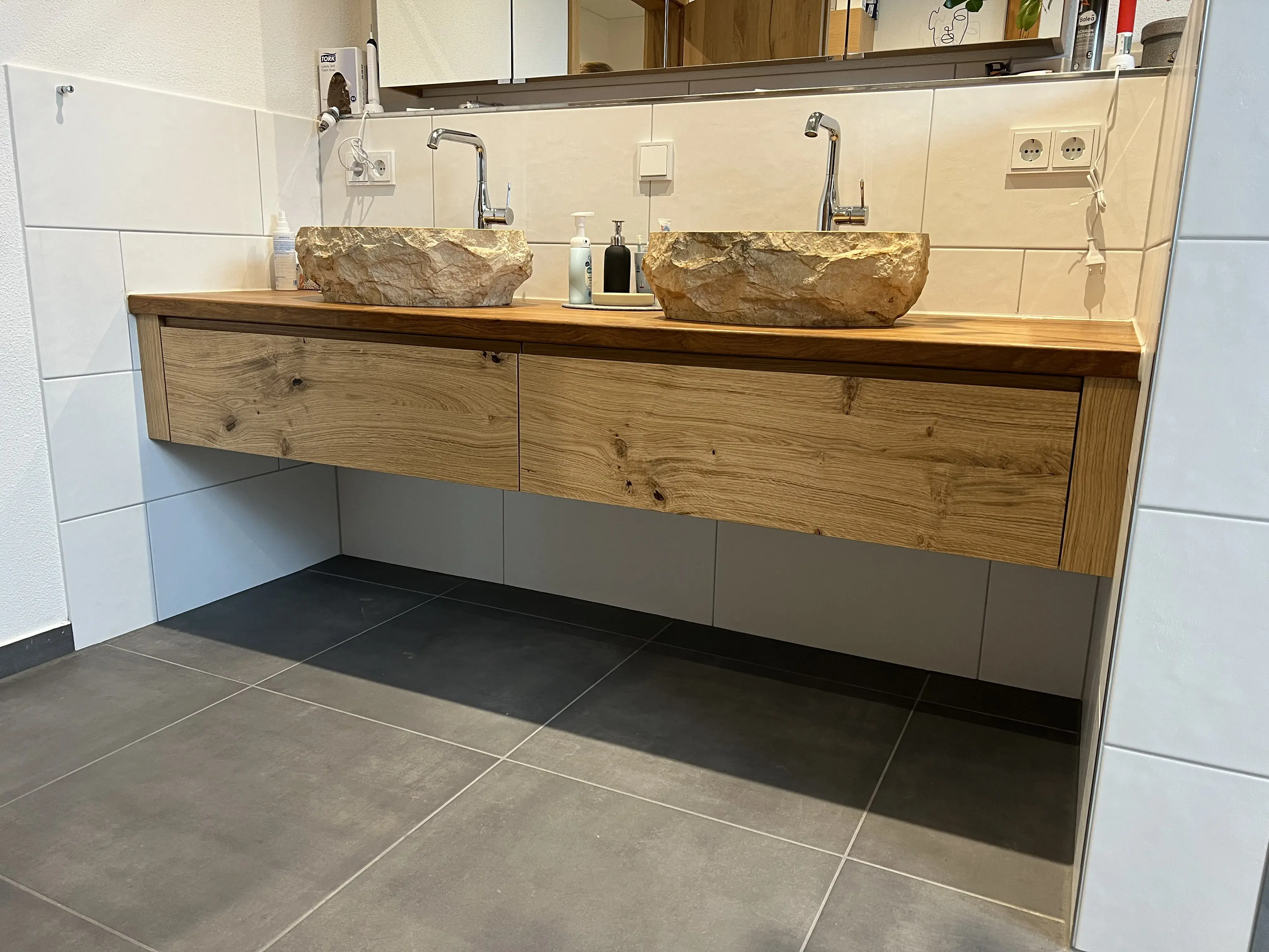 Zwei steinerne Waschbecken auf Holzwaschtisch mit Spiegel im modernen Bad.