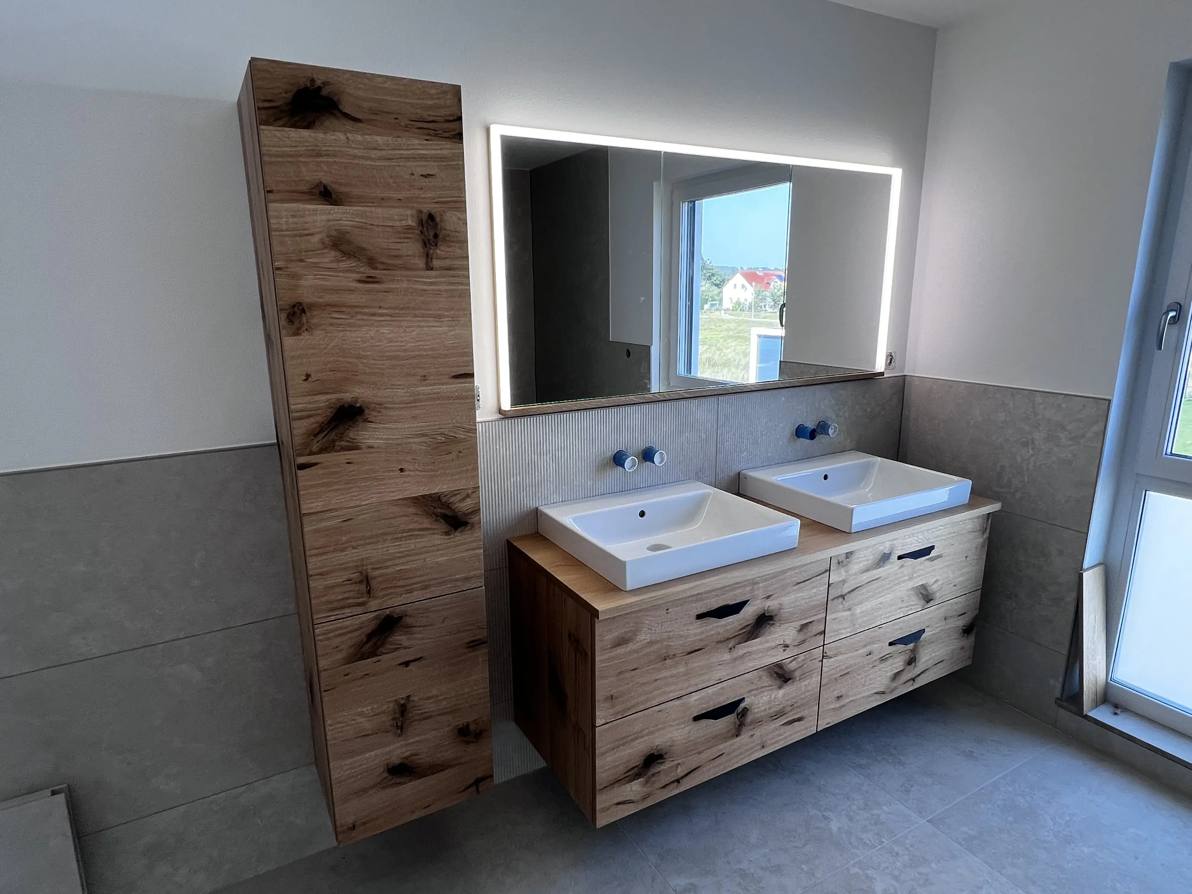 Modernes Badezimmer mit Holzschrank, Doppelwaschbecken und beleuchtetem Spiegel.