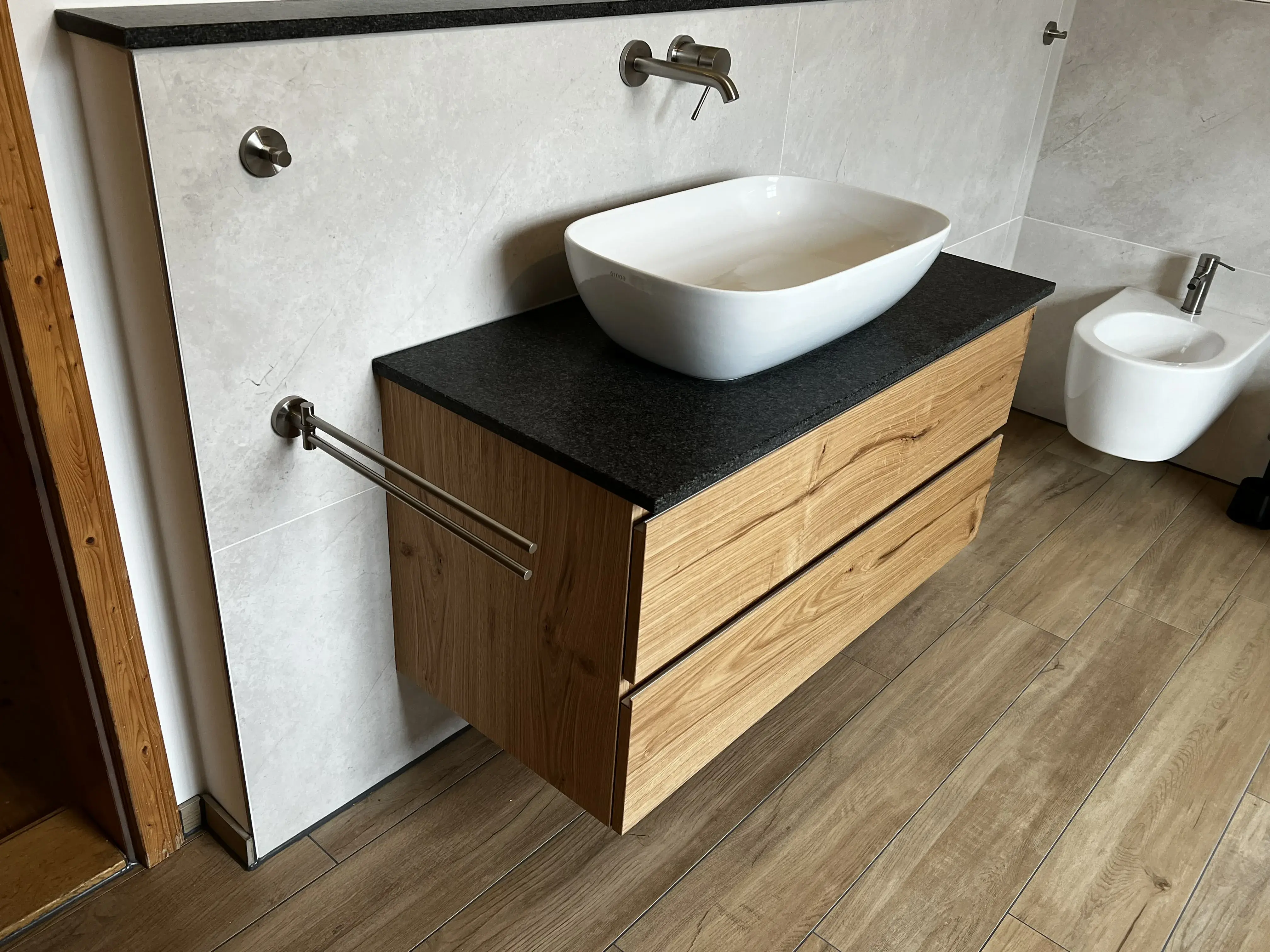 Waschbecken auf Holzunterschrank mit schwarzer Platte, daneben ein modernes WC.