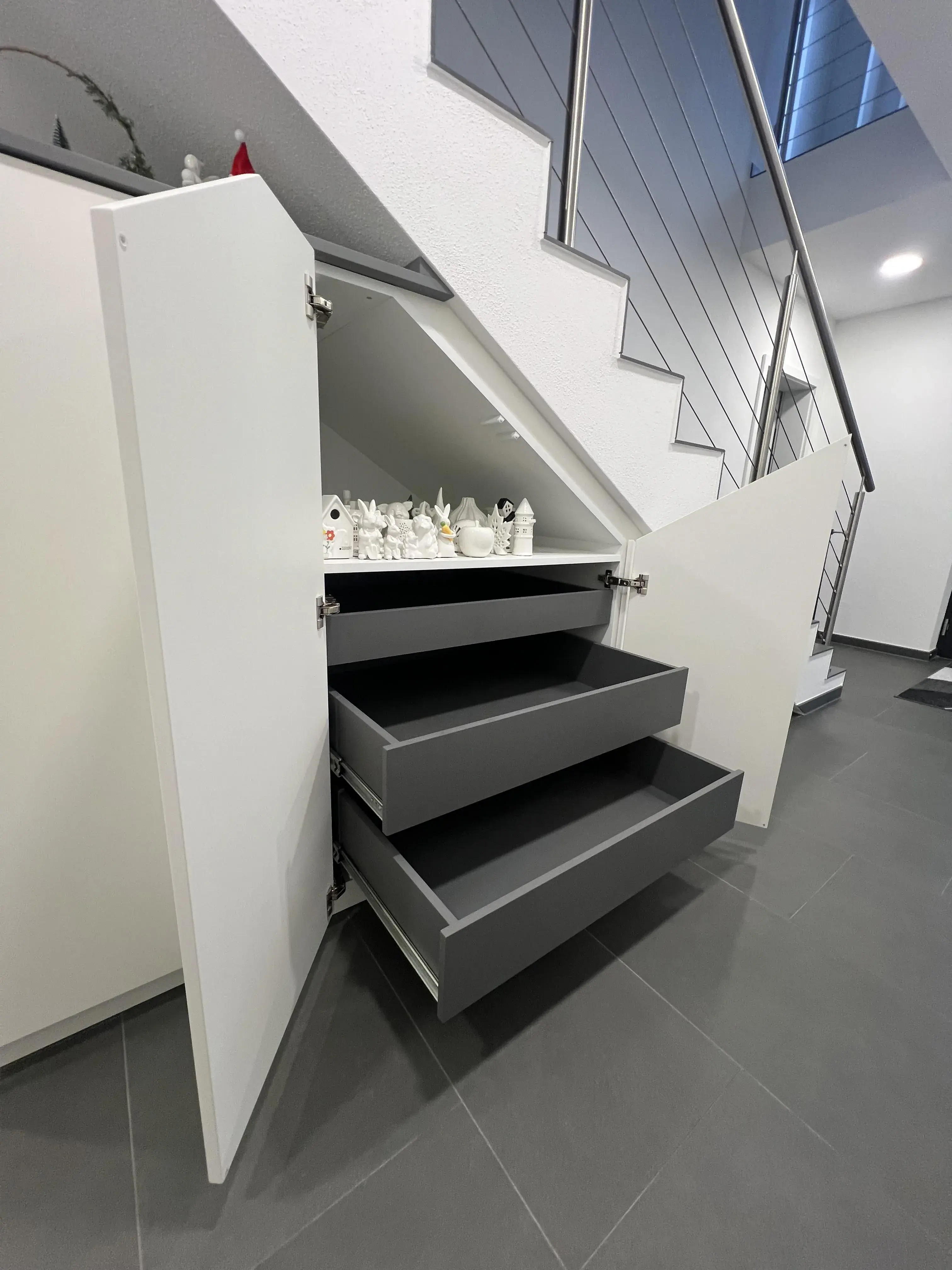 Drei offene Schubladen unter einer Treppe, modern eingerichtet.