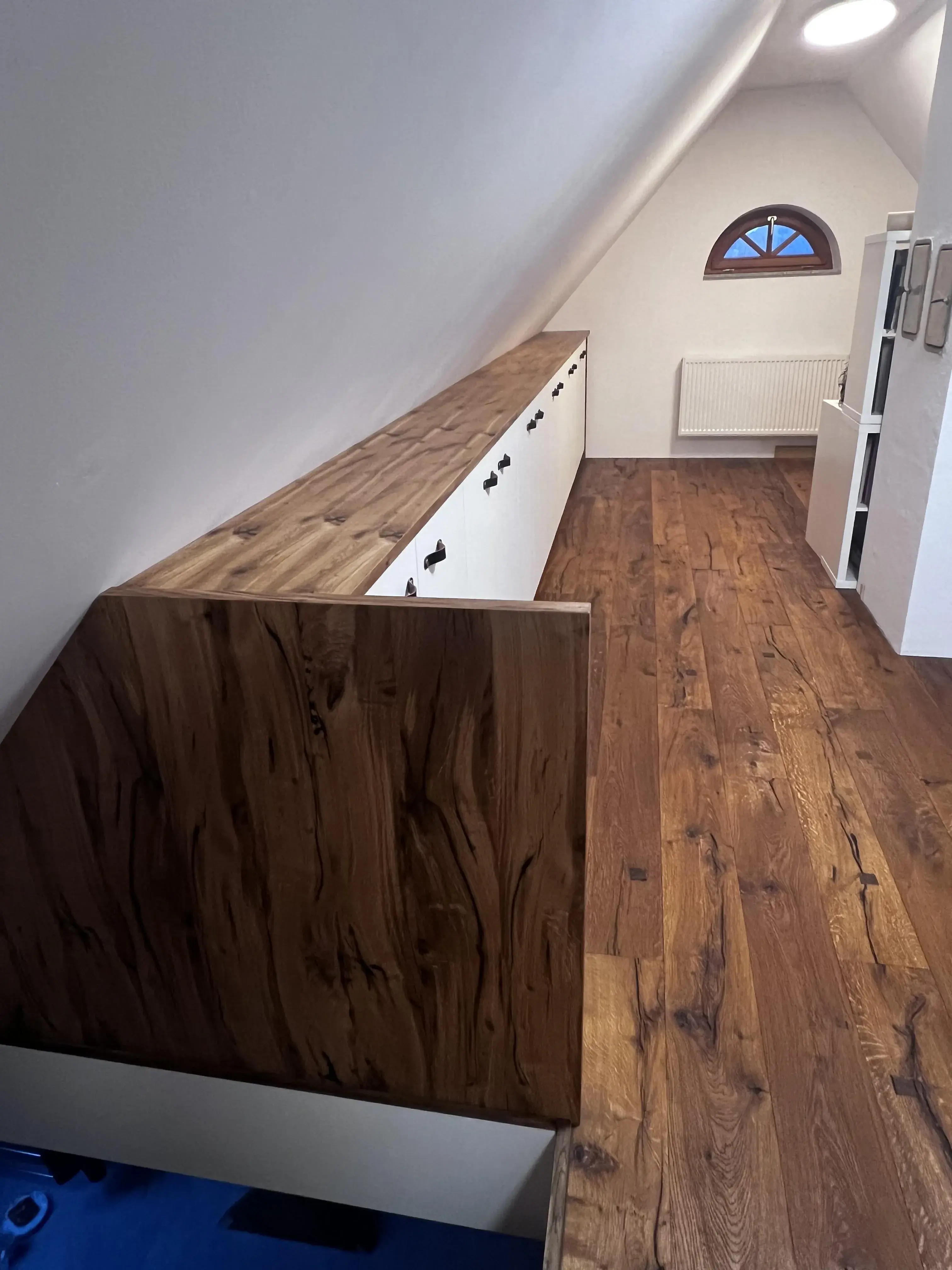 Dachzimmer mit Holzfußboden, langer Einbauschrank und kleinem Rundfenster