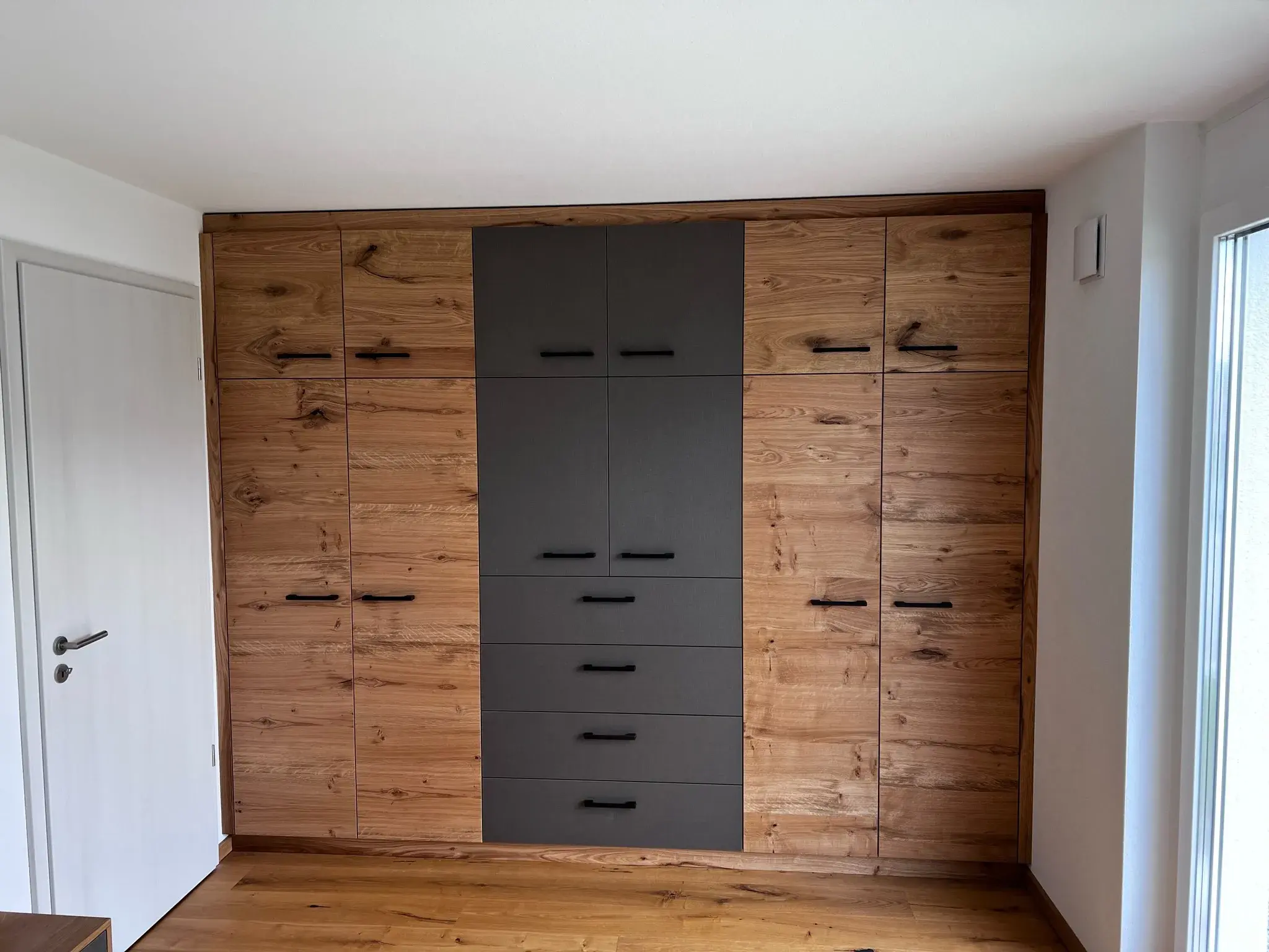 Großer Einbauschrank aus Holz mit schwarzen Schubladen in einem hellen Raum.