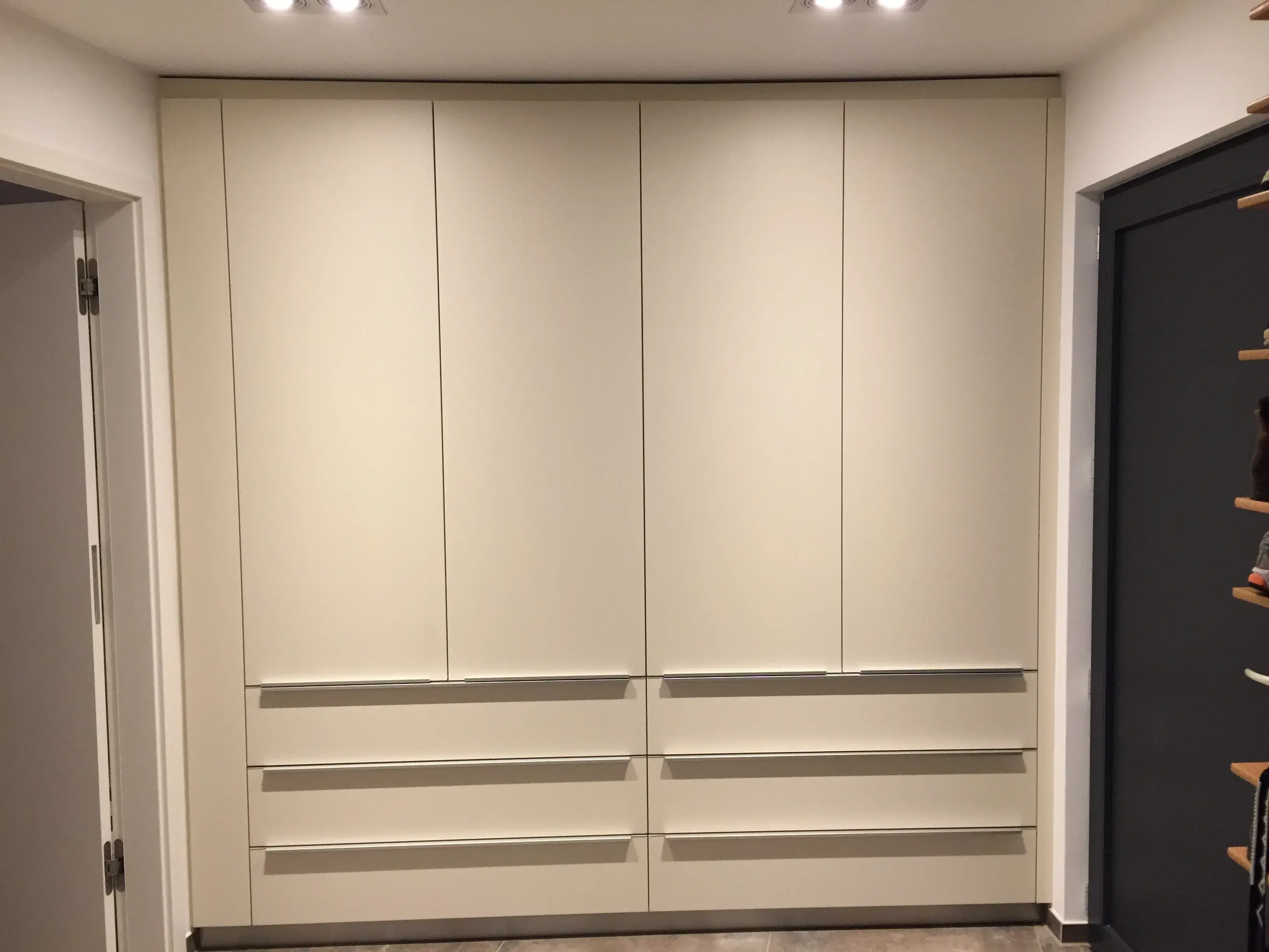 Großer, moderner Einbauschrank mit weißen Türen und Schubladen unter heller Deckenbeleuchtung.