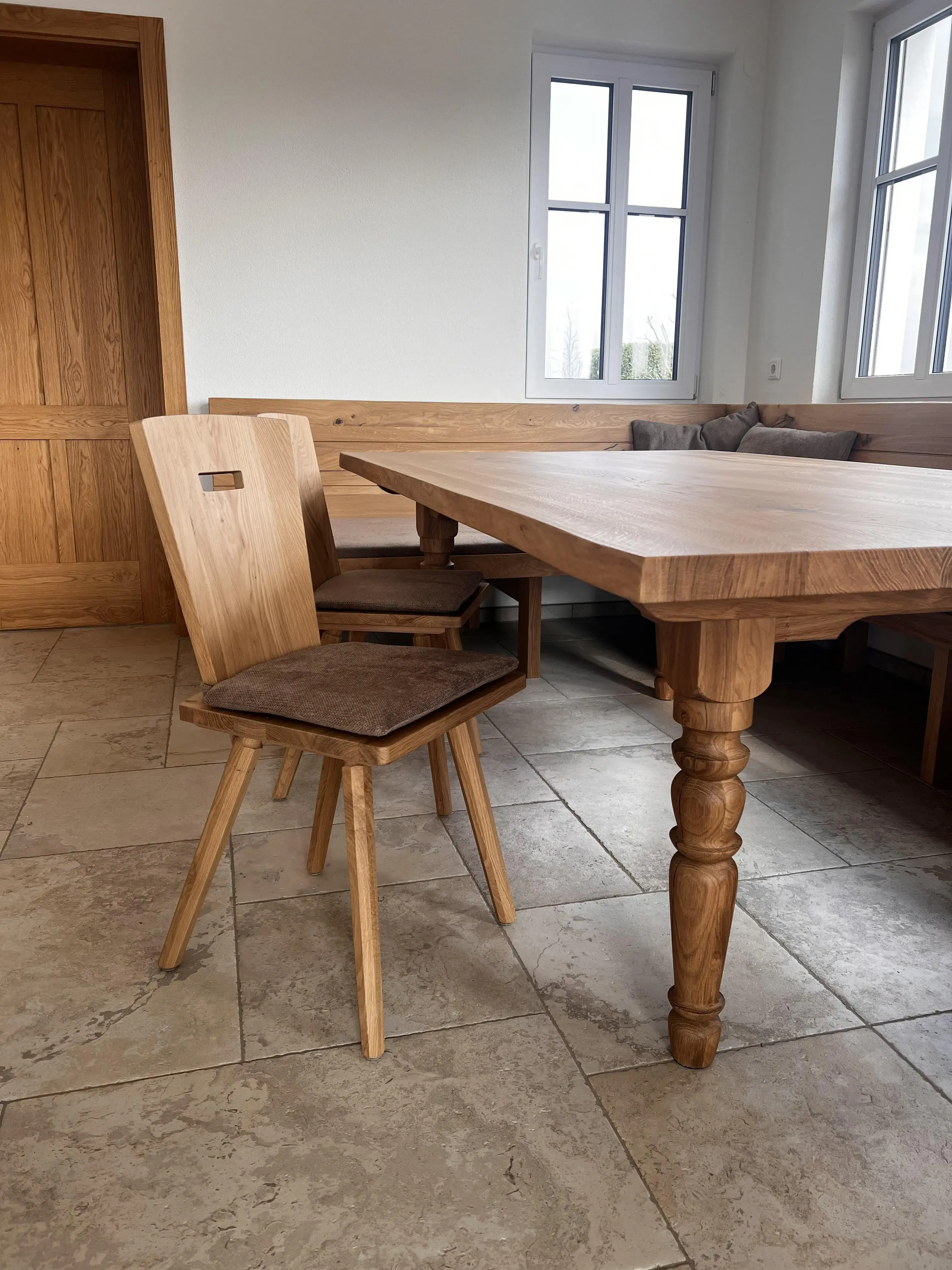 Holztisch mit zwei Stühlen in einem hellen Raum mit Fliesenboden und Fenster.