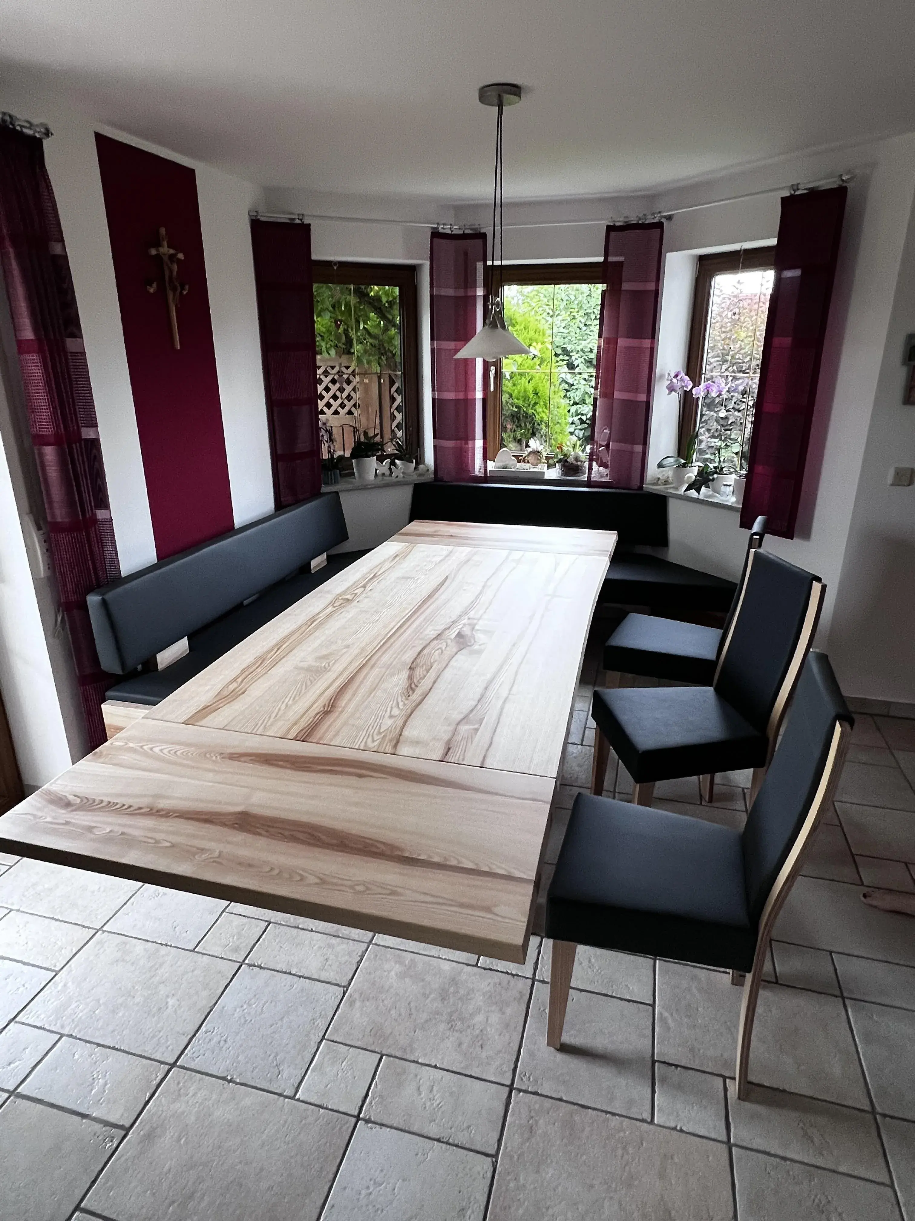 Esstisch mit Holzplatte, Eckbank und drei schwarzen Stühlen in einem hellen Esszimmer.