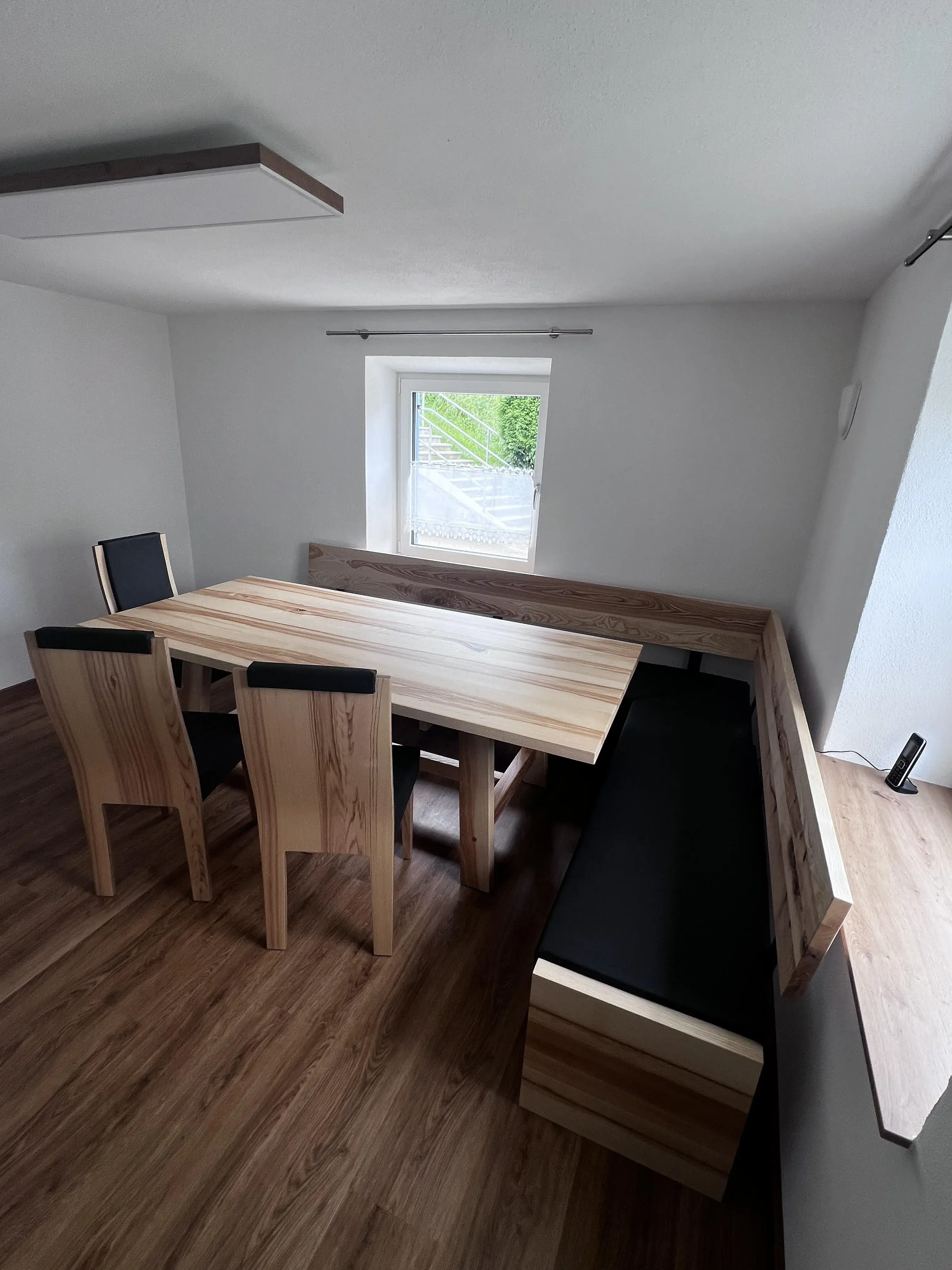Holztisch mit Eckbank und zwei Stühlen in einem hellen Raum mit Fenster.