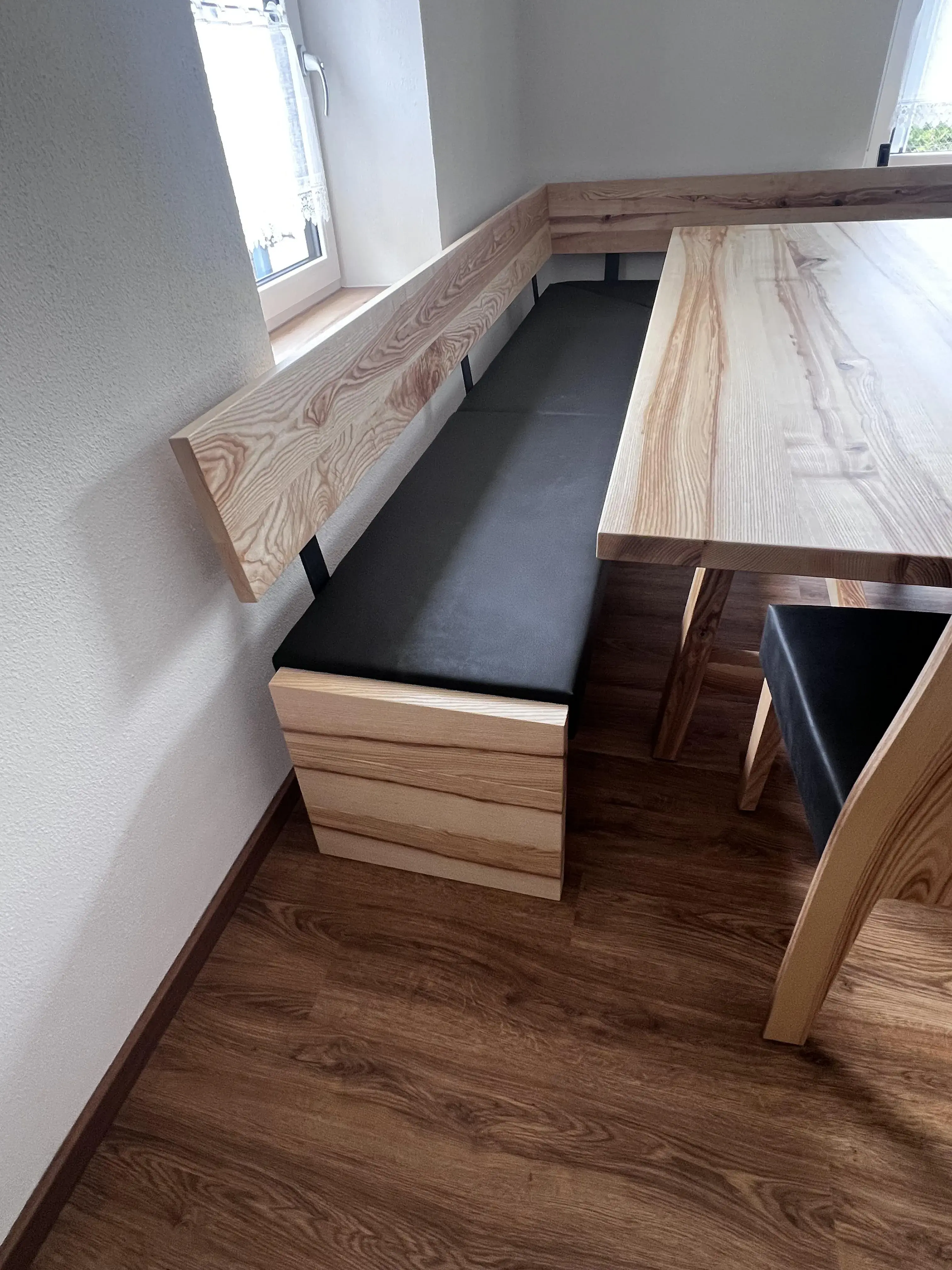 Eckbank aus Holz mit schwarzem Polster neben einem Holztisch auf Laminatboden