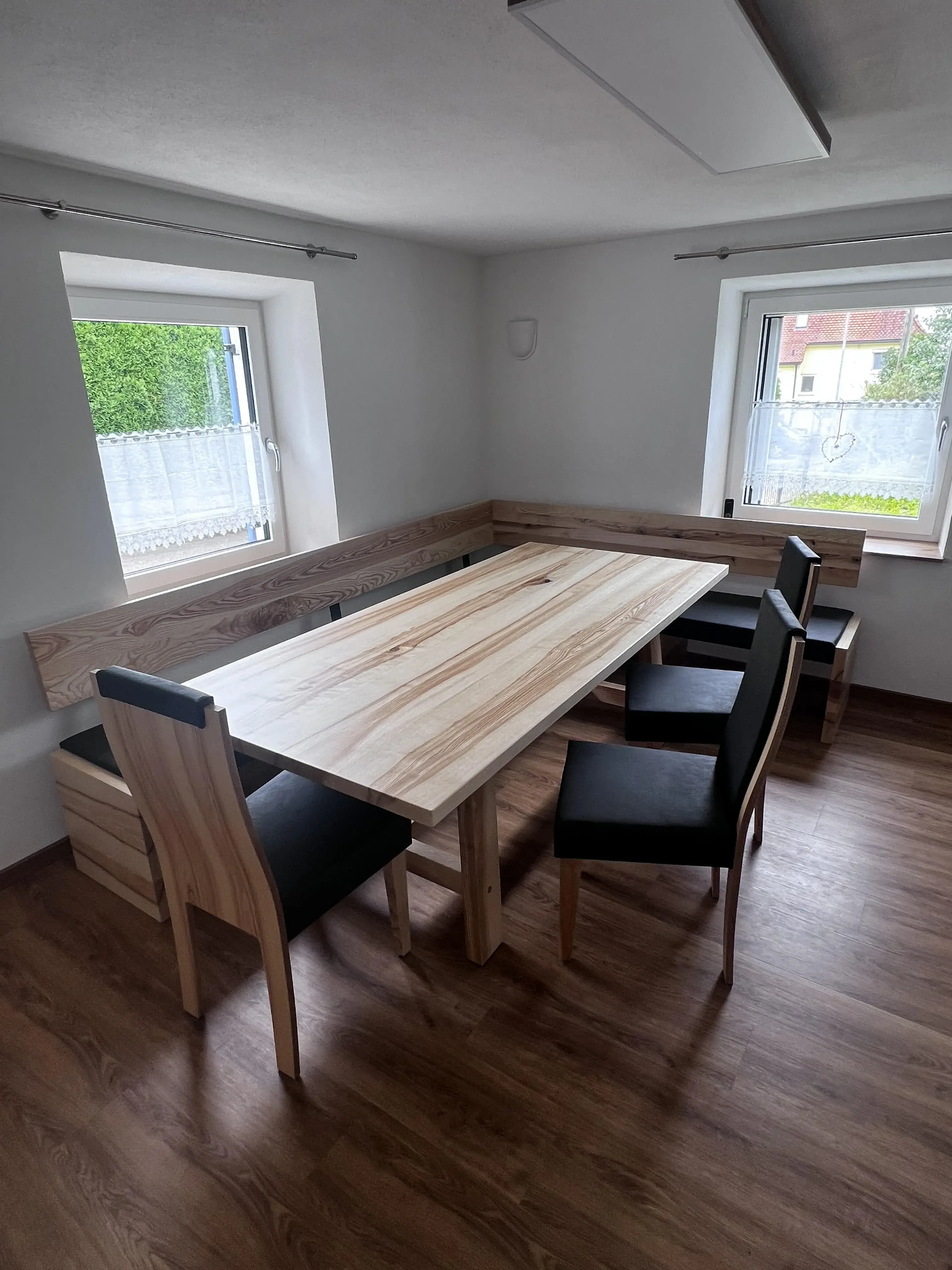 Heller Essbereich mit Holztisch, Eckbank und schwarzen Stühlen auf Laminatboden.