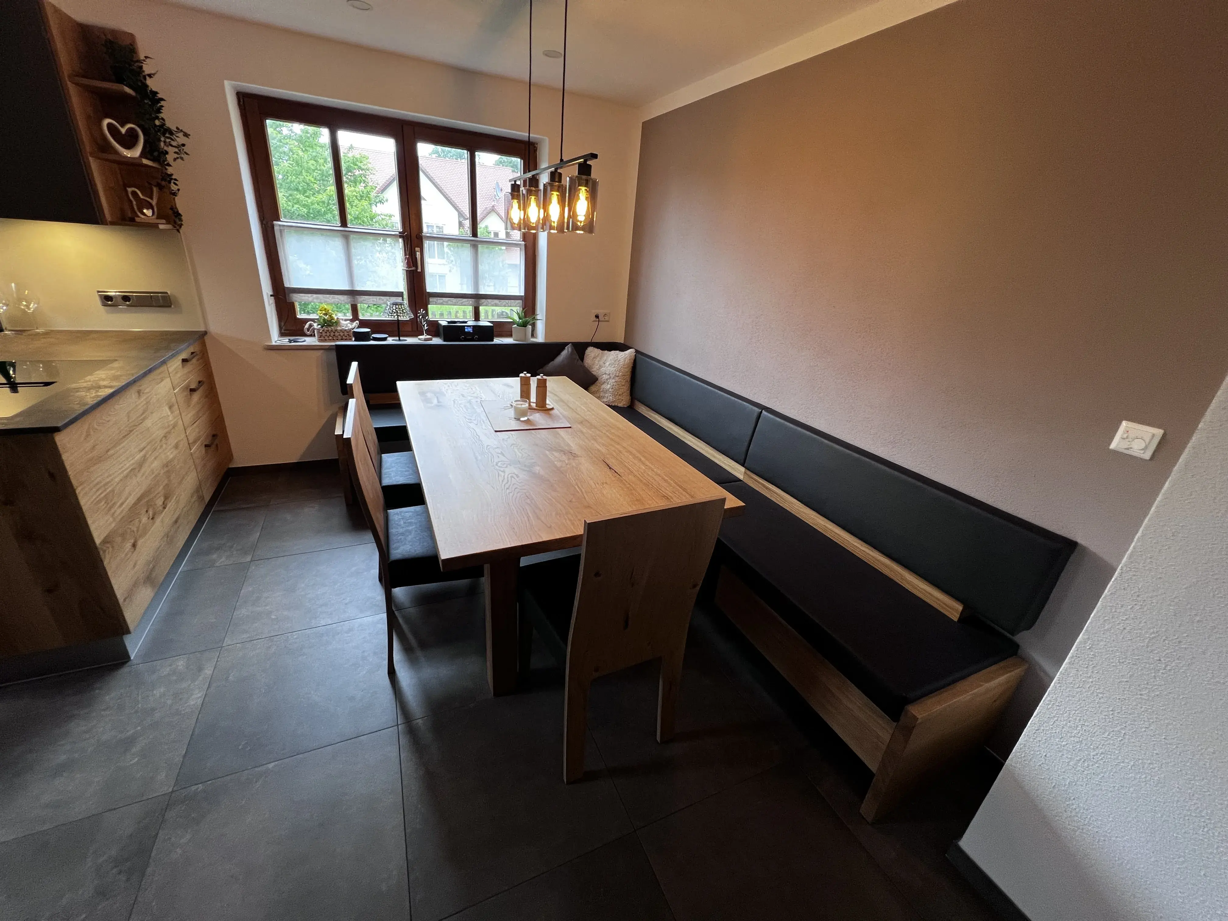 Essbereich mit Holztisch, Stühlen und Eckbank, große Fenster, moderne Hängelampen.