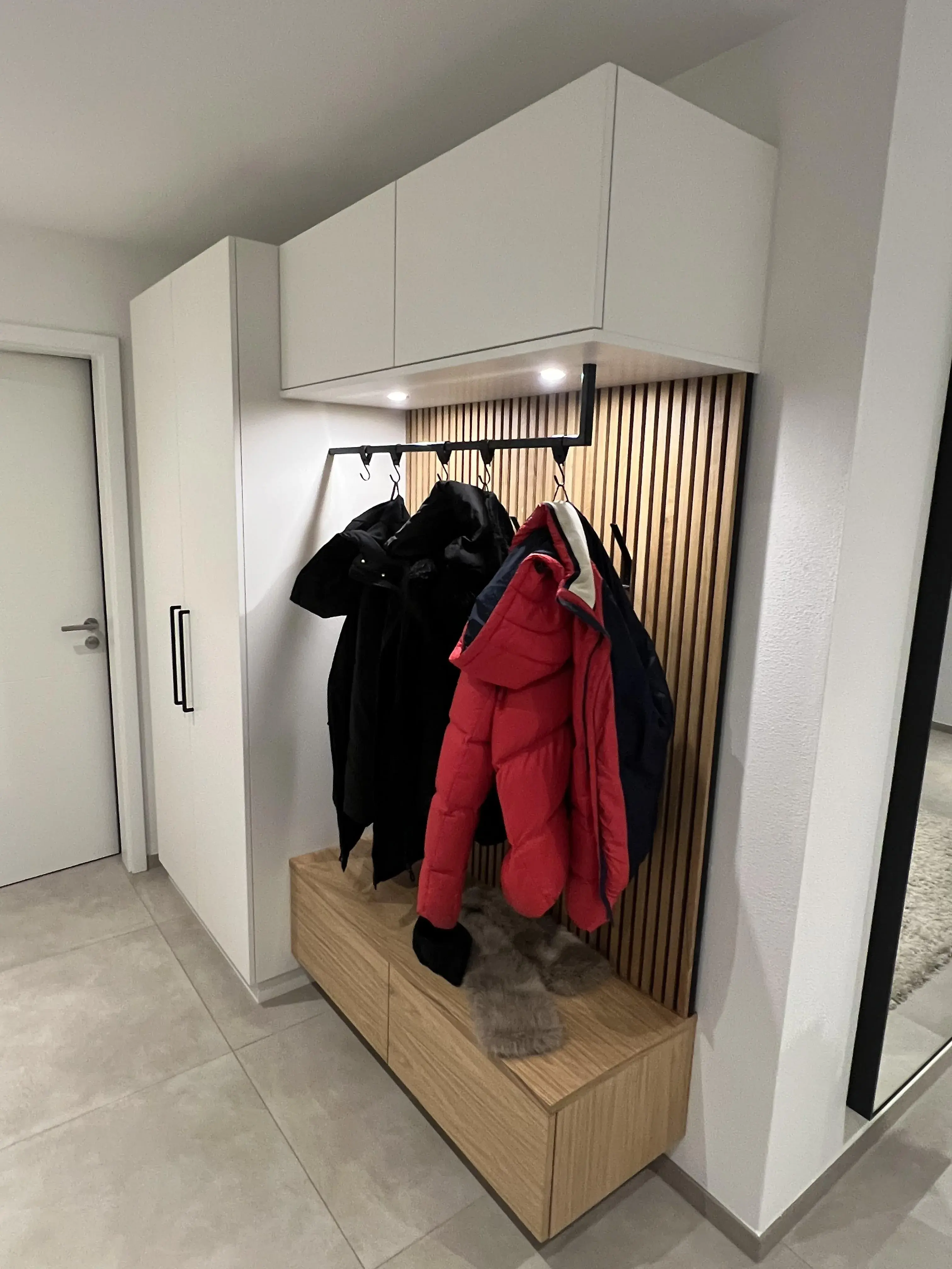 Garderobe mit Jacken, Holzbänken und weißen Schränken in modernem Flur.
