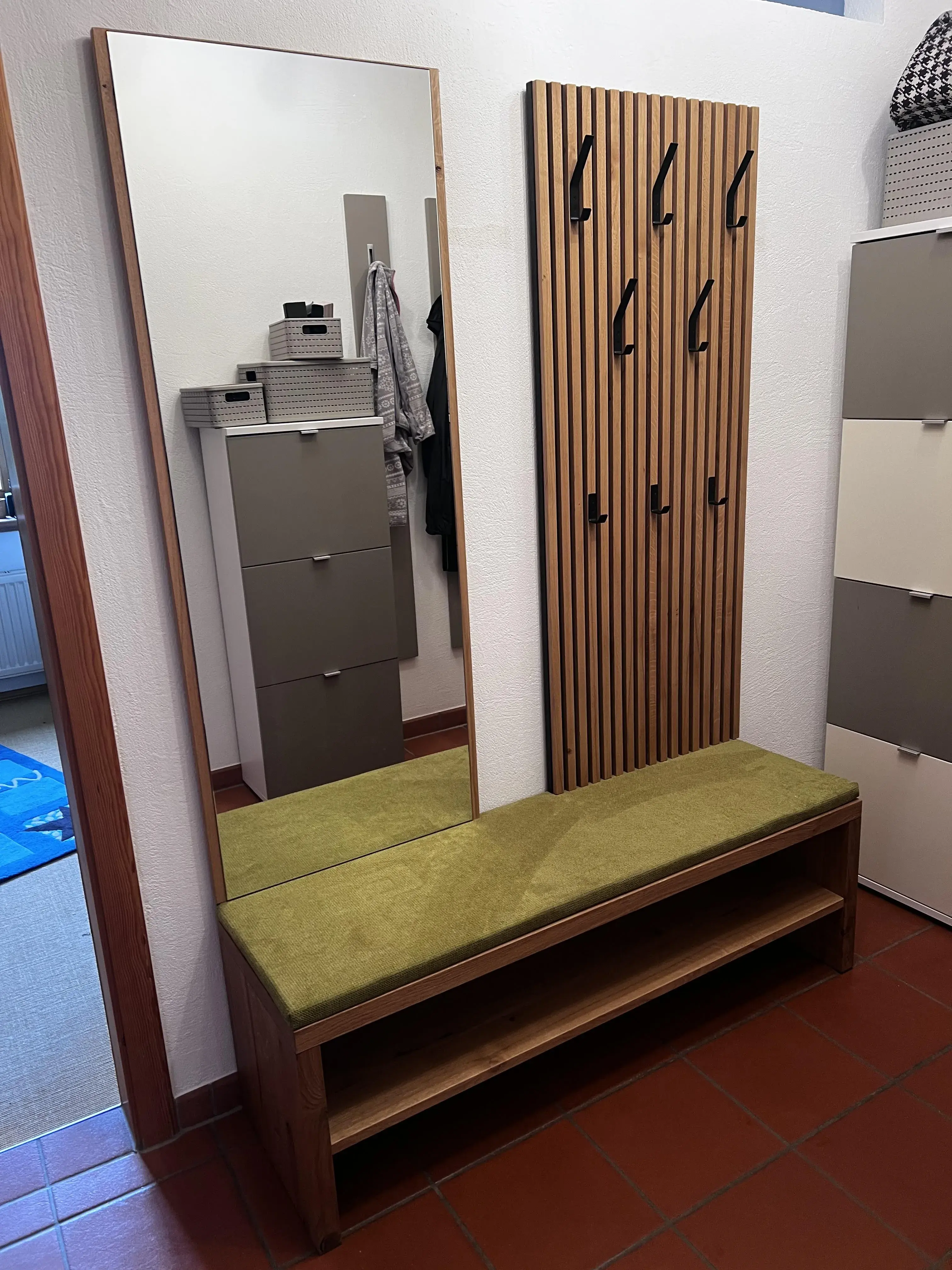 Flurbank mit grünem Polster, großem Spiegel und Holz-Garderobe mit Haken.