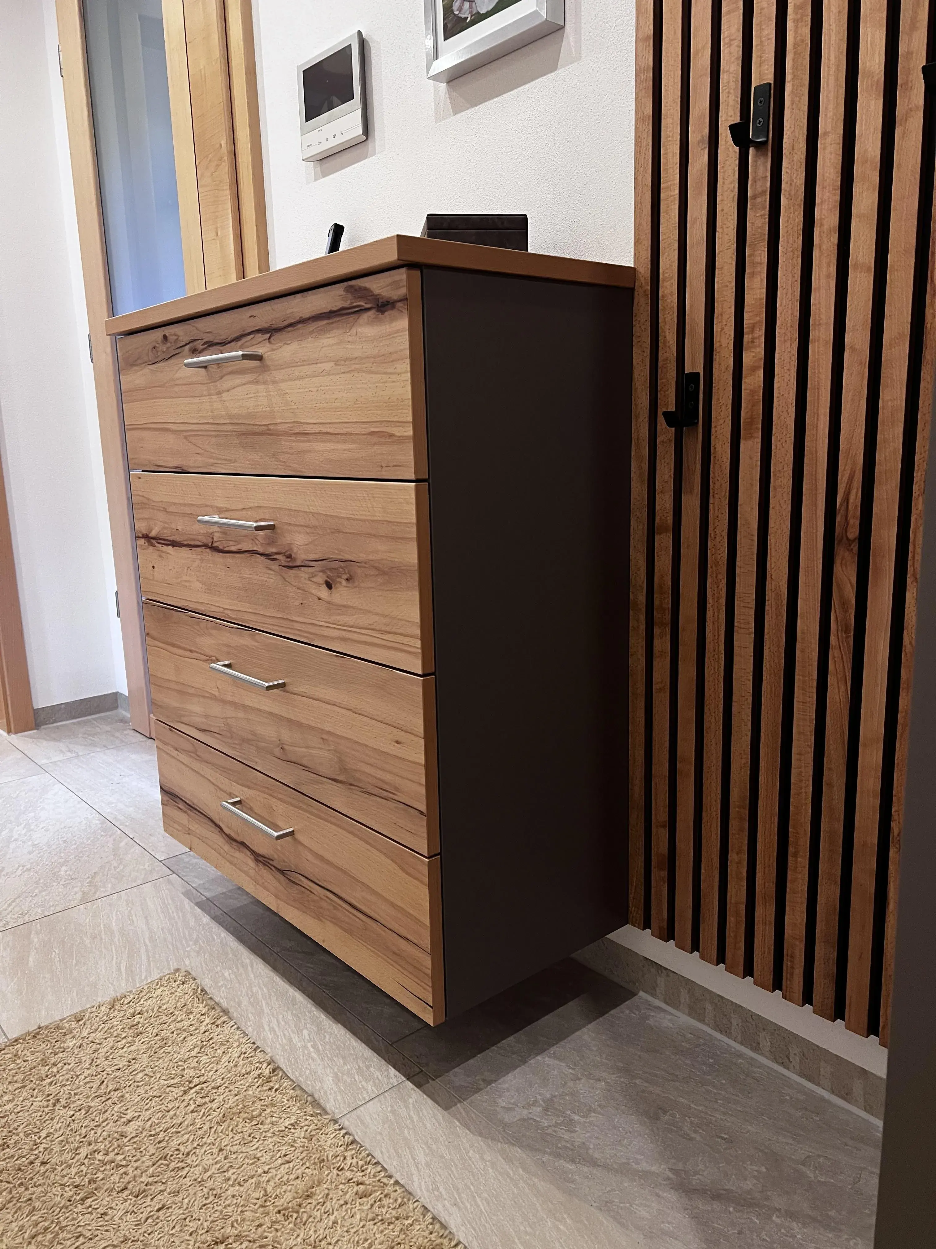 Holzkommode mit vier Schubladen in modernem Flur, helle Fliesen und Wandverkleidung.