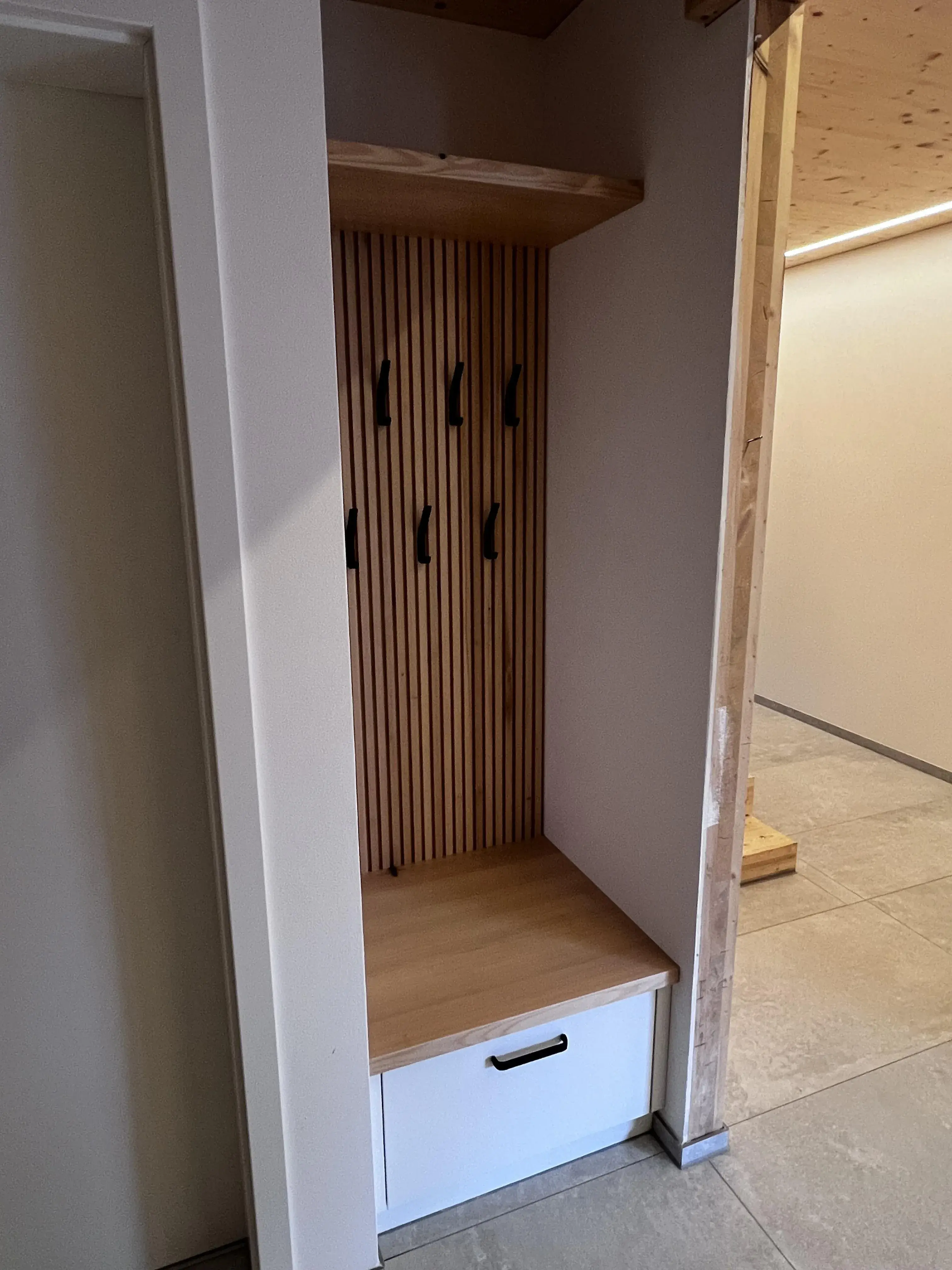 Offene Garderobe aus Holz mit Sitzbank, Haken und einer Schublade.