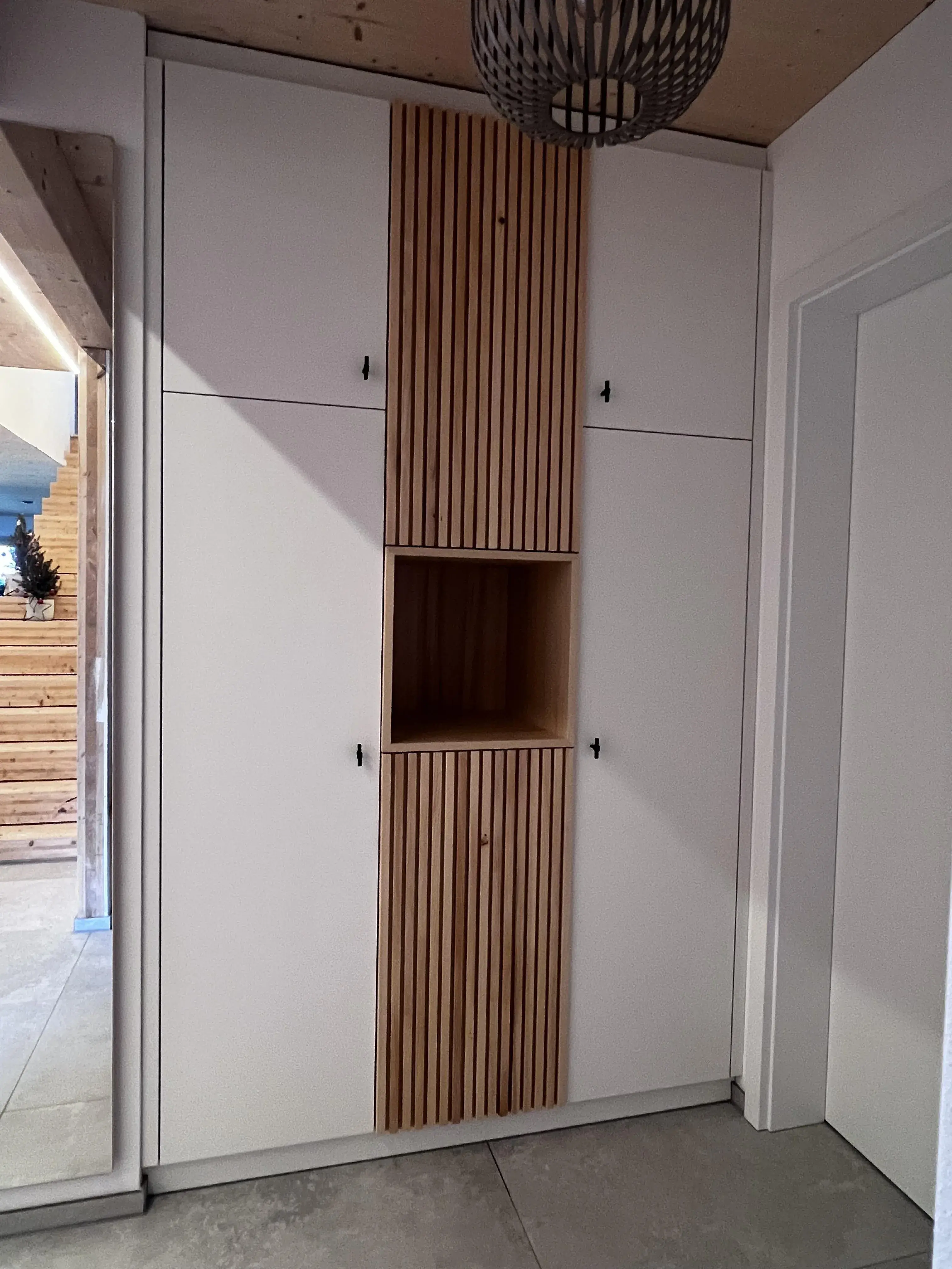 Weißer Einbauschrank mit vertikalen Holzelementen und offenem Fach in der Mitte.