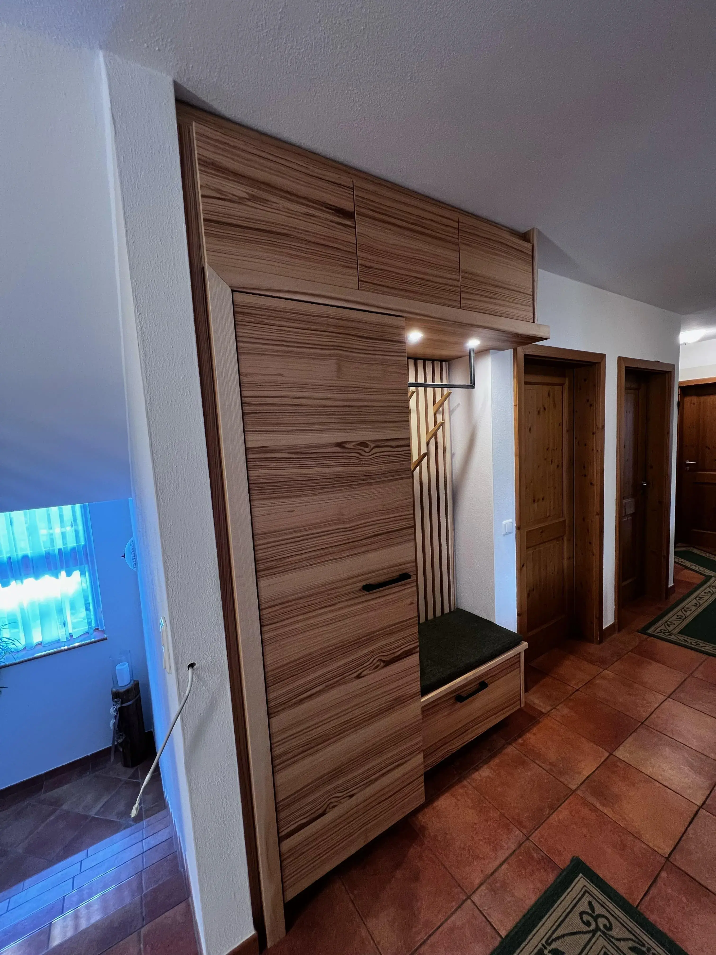 Holzgarderobe mit Sitzbank und Kleiderhaken in einem Flur mit Fliesenboden
