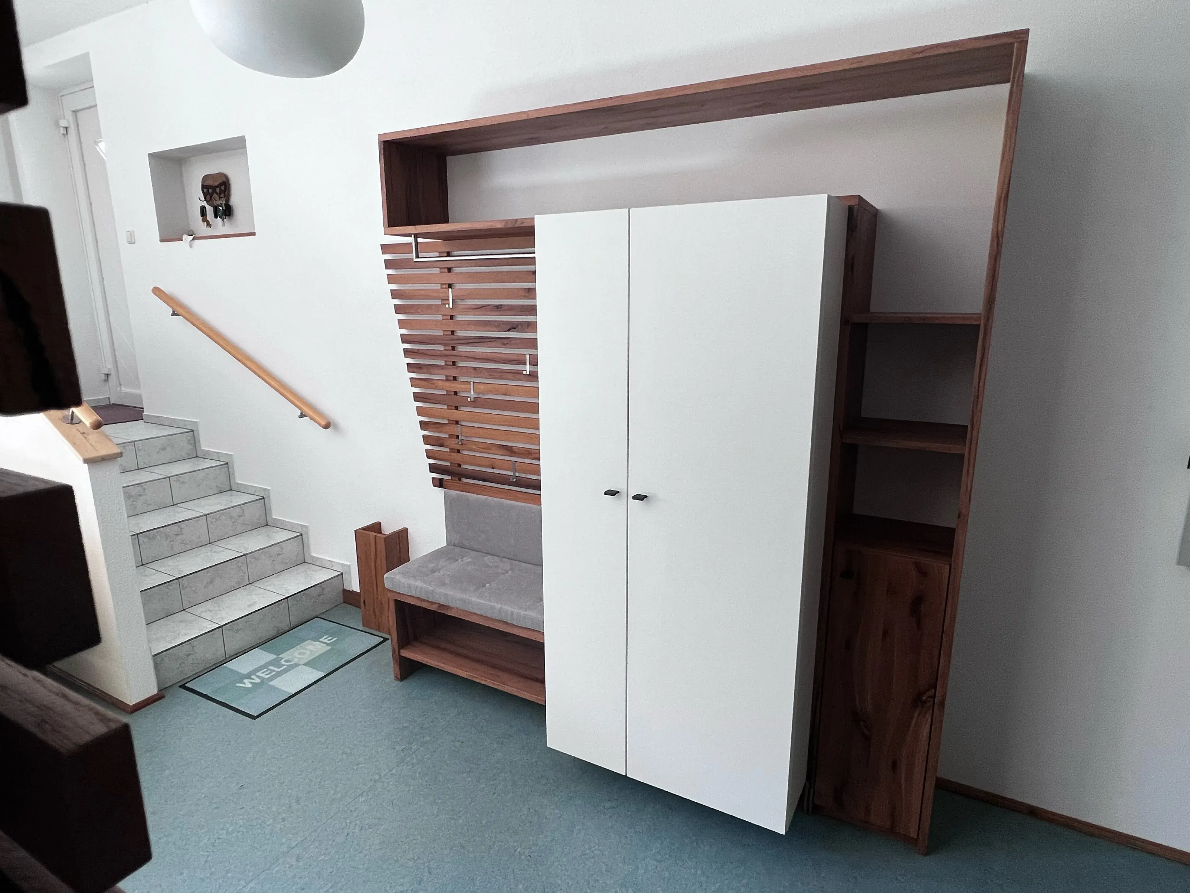 Moderner Flur mit Holz-Garderobe, weißen Türen und Sitzbank neben Treppe.
