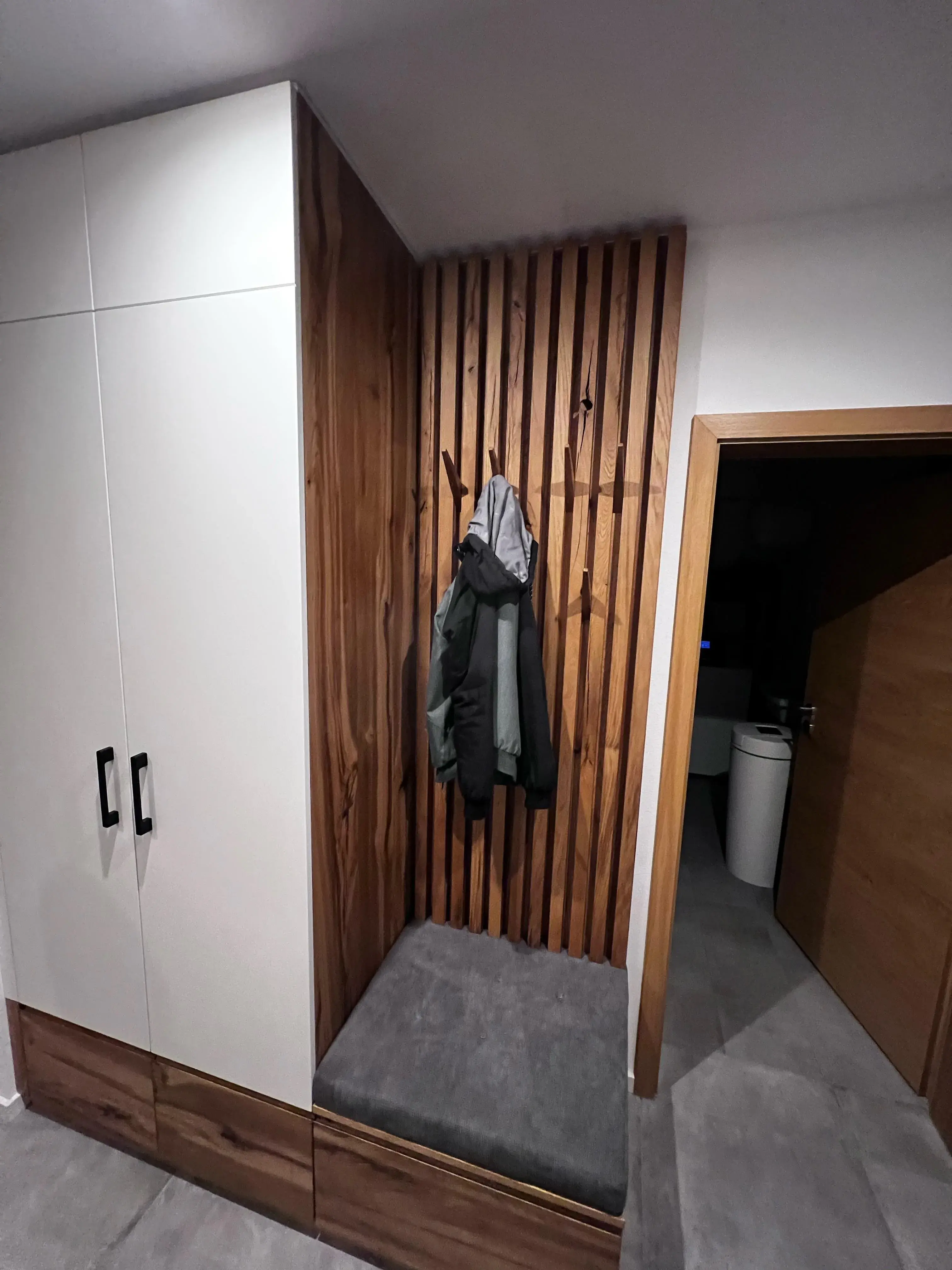 Garderobe mit Holzwand, grauem Sitzpolster und aufgehängter Jacke im Flur