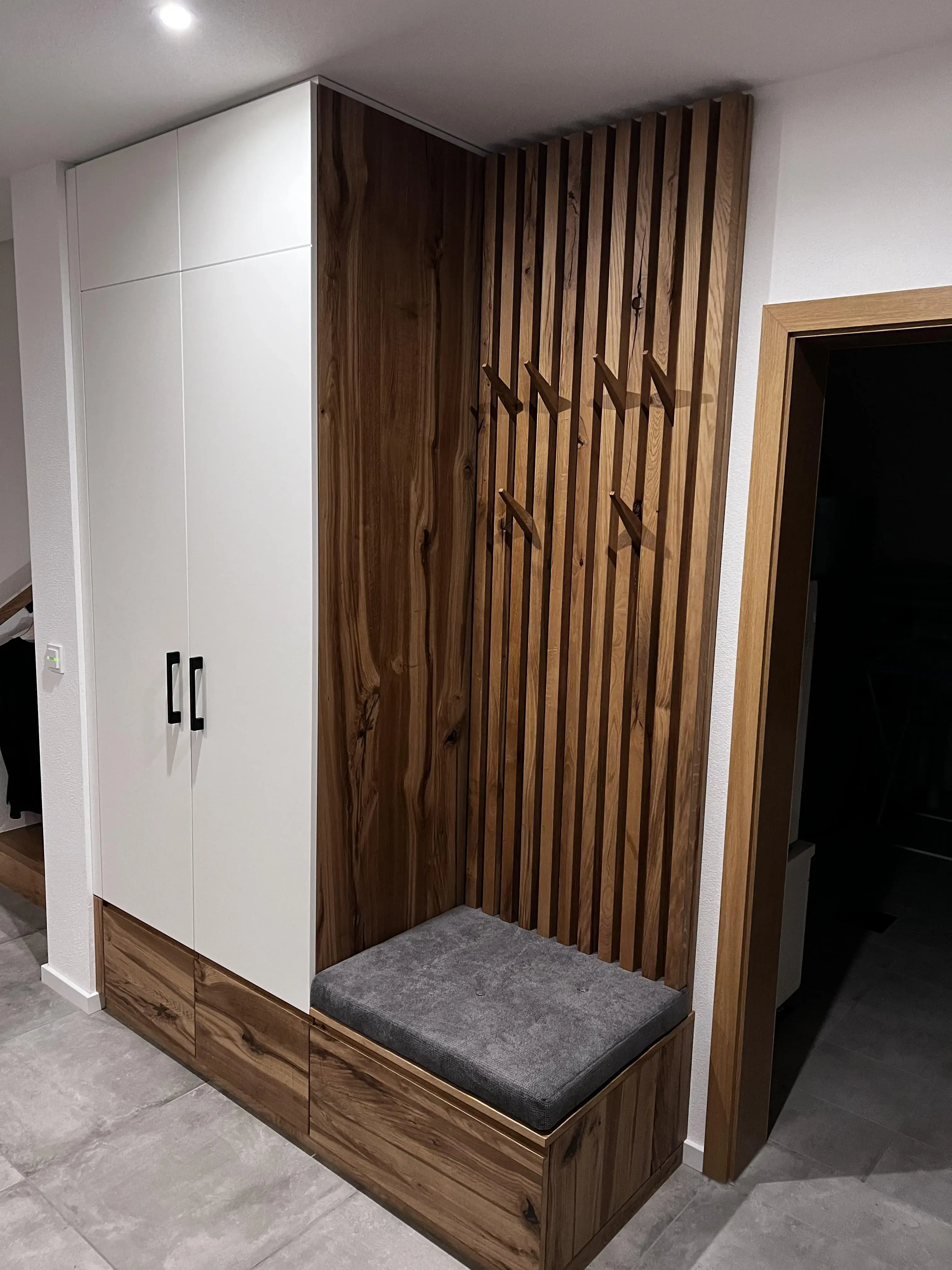 Garderobe mit weißem Schrank, Holzlattenwand und grauer Sitzbank