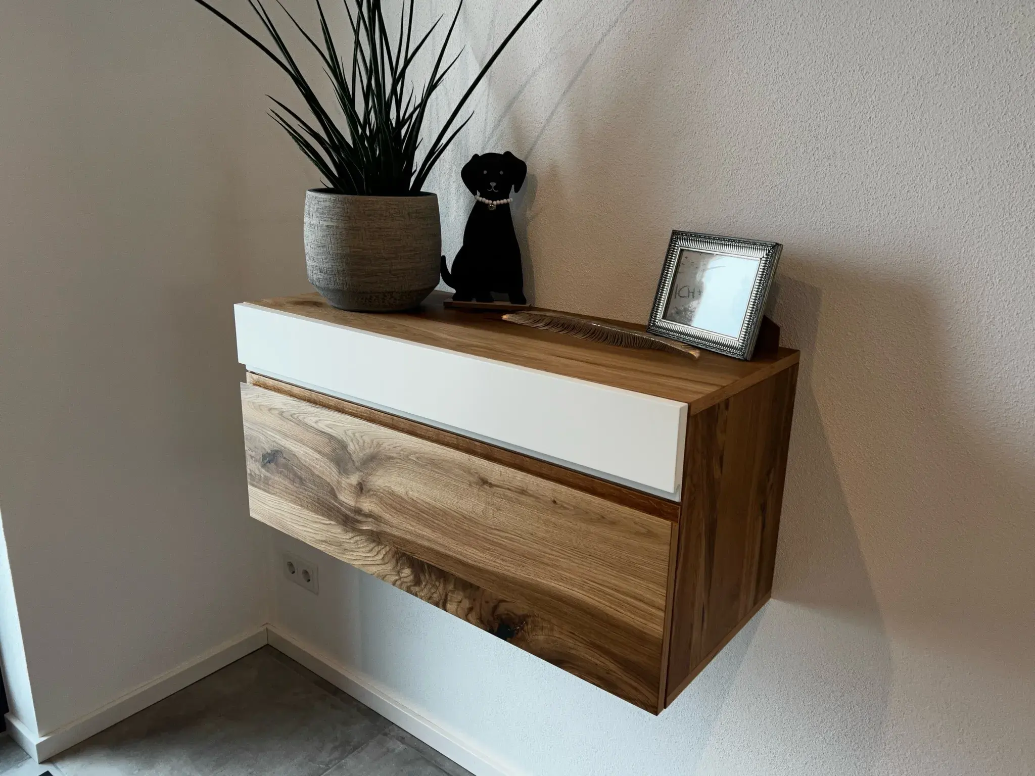 Holzkommode an der Wand mit Pflanze, Dekofigur und gerahmtem Foto.