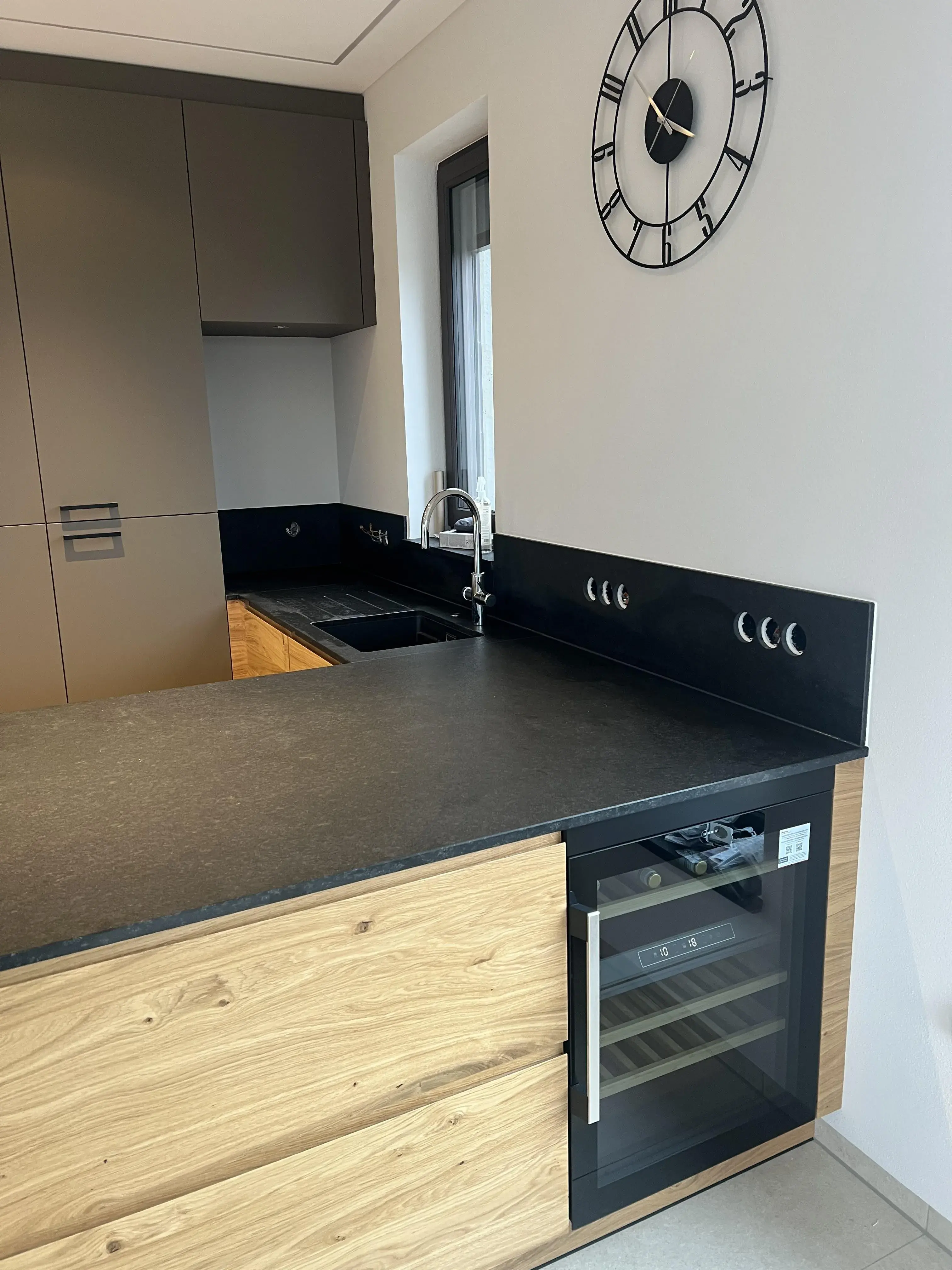 Moderne Küche mit schwarzer Arbeitsplatte, Holzfronten und Wand-Uhr.