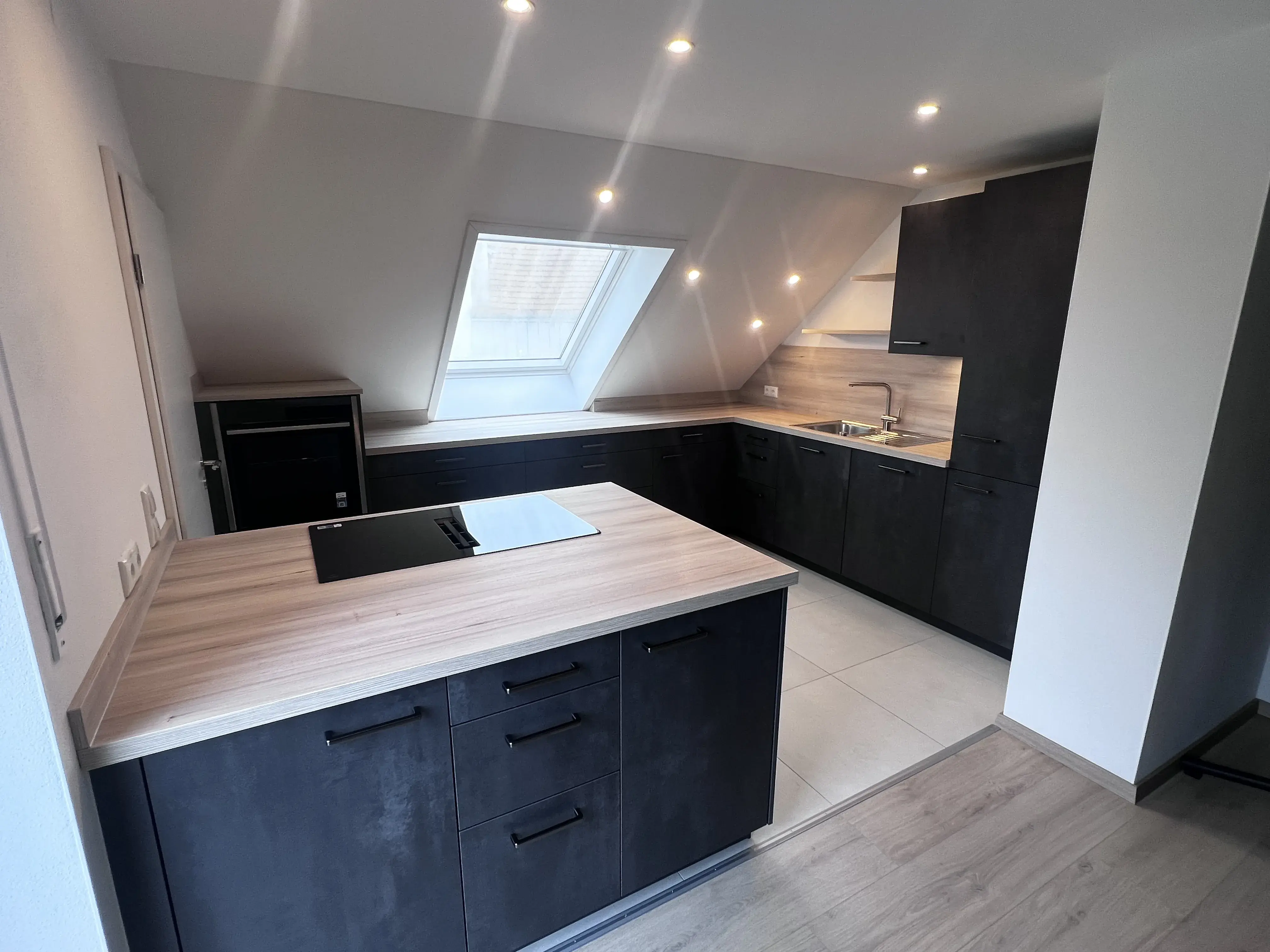 Moderne Küche mit dunklen Schränken, Holzarbeitsplatten und Dachfenster.