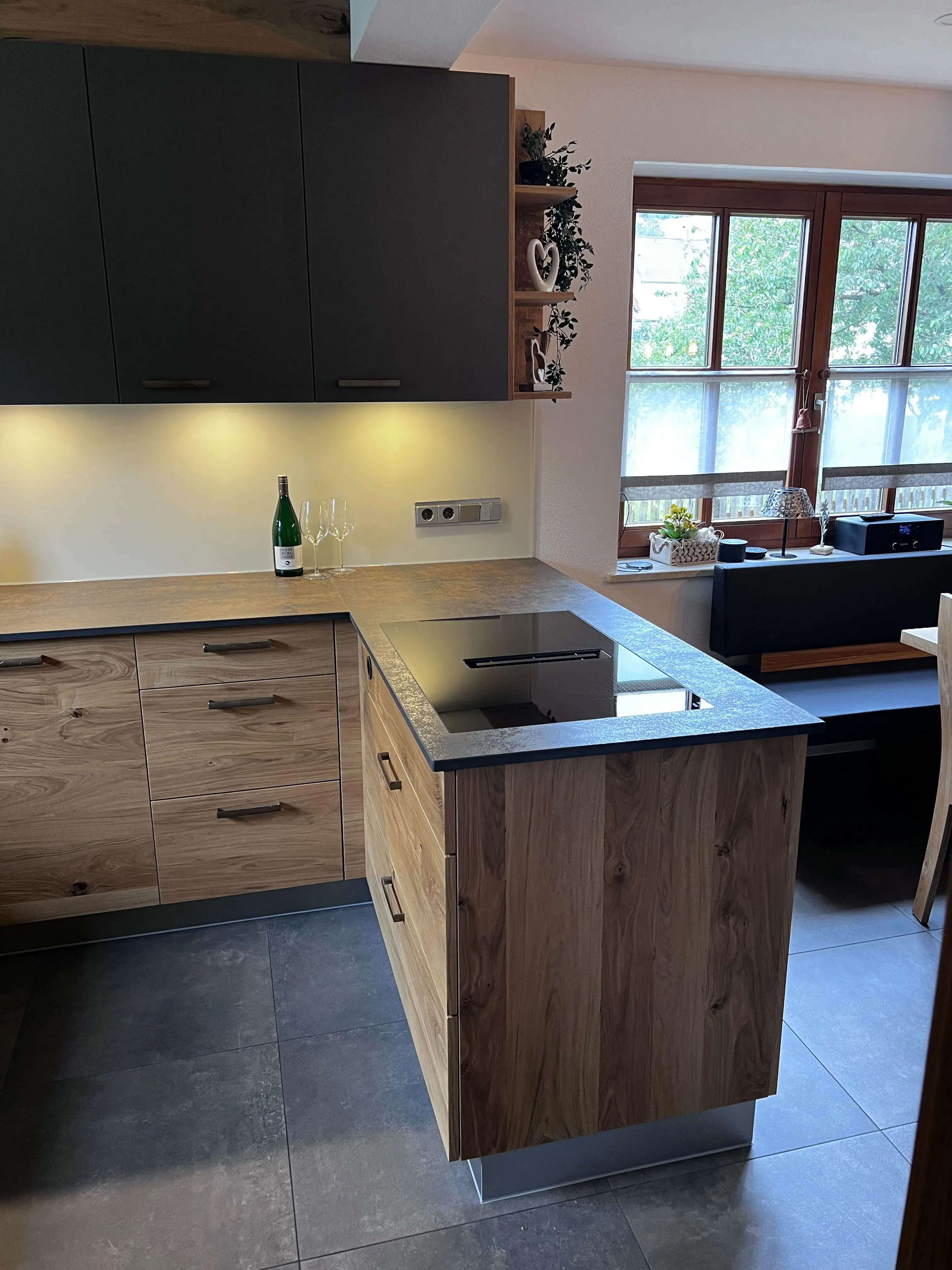 Moderne Küche mit Kochinsel, Holzfronten und großen Fenstern im Hintergrund.