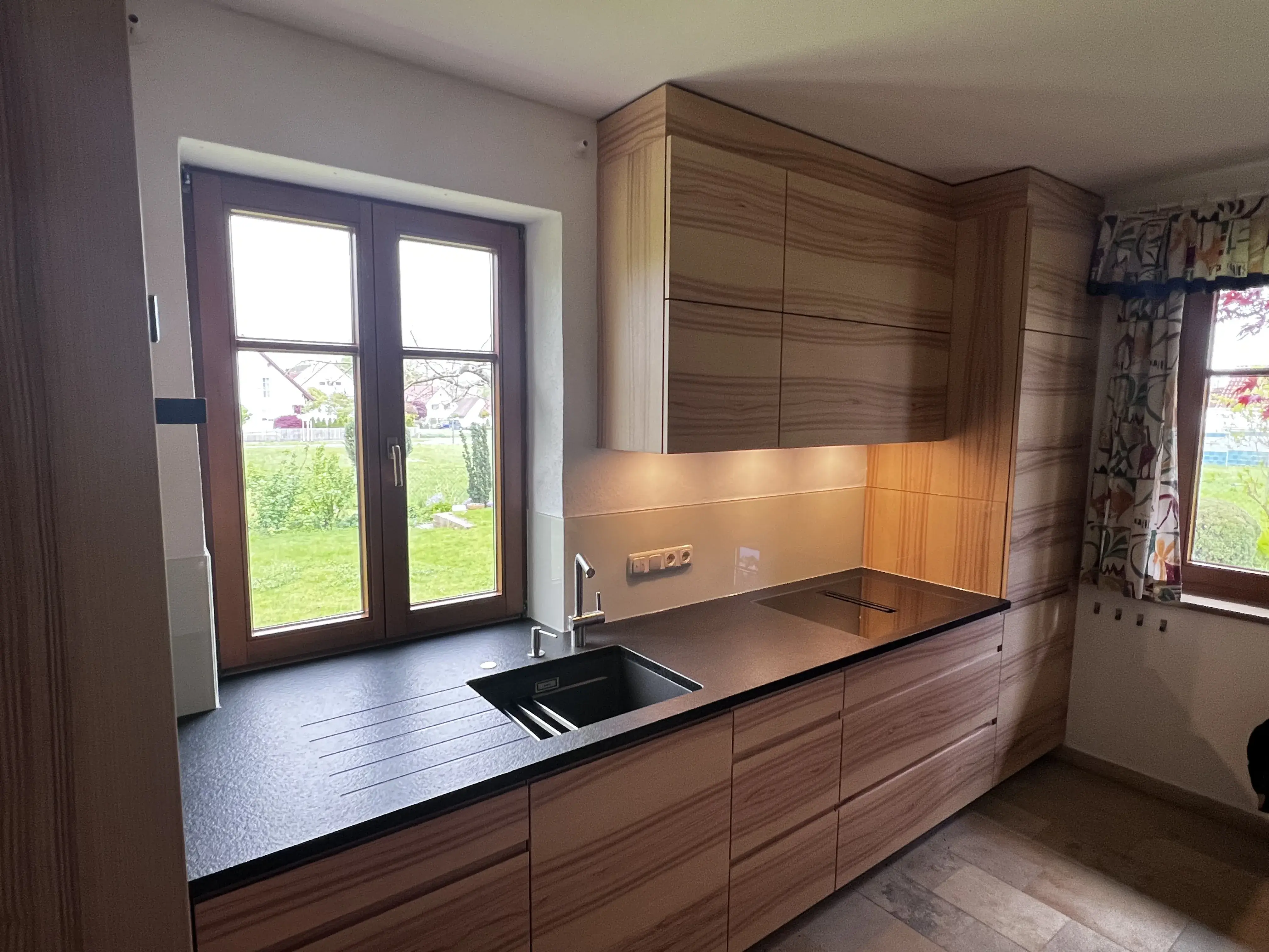 Moderne Holzküche mit schwarzer Arbeitsplatte und Spülbecken, Fenster mit Blick ins Grüne.