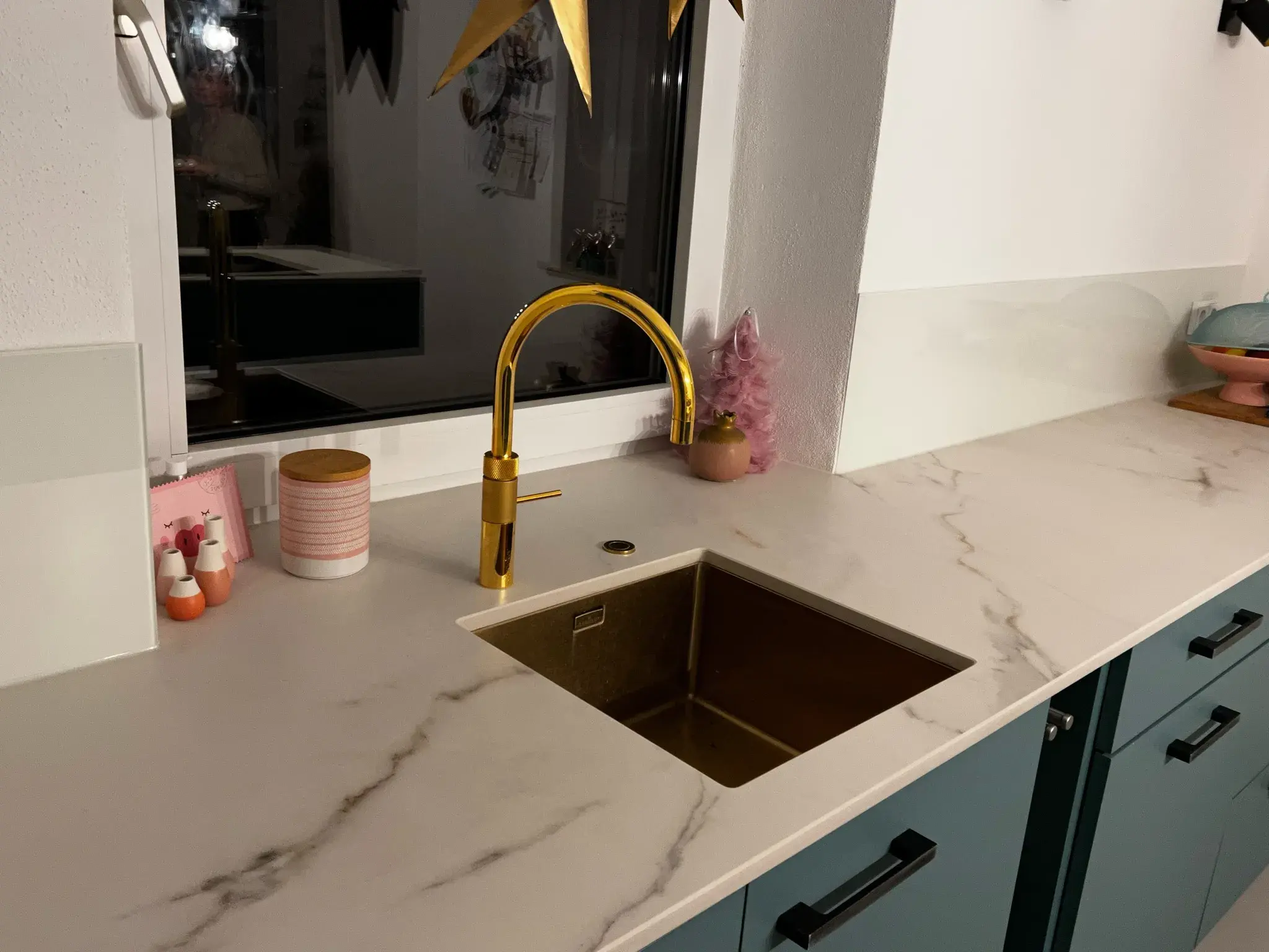 Moderne Küche mit goldener Spüle und Wasserhahn auf weißer Marmorarbeitsplatte.