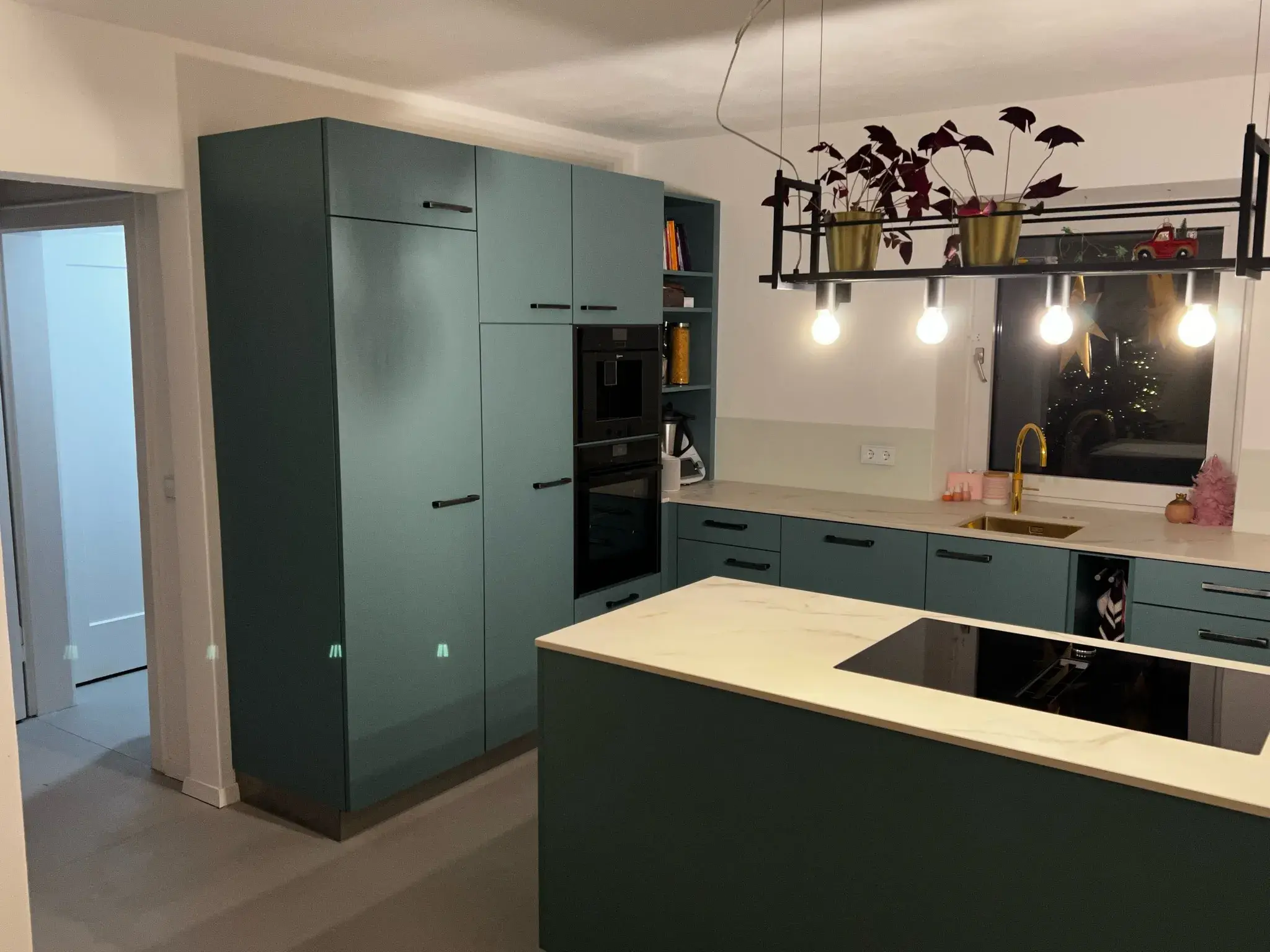 Moderne Küche mit grünen Schränken, Kochinsel und hängenden Lampen.