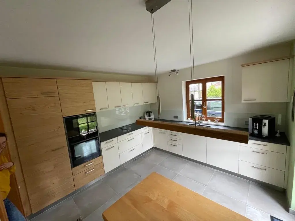 Moderne Küche mit Holzmöbeln, weißen Schränken und großem Fenster.