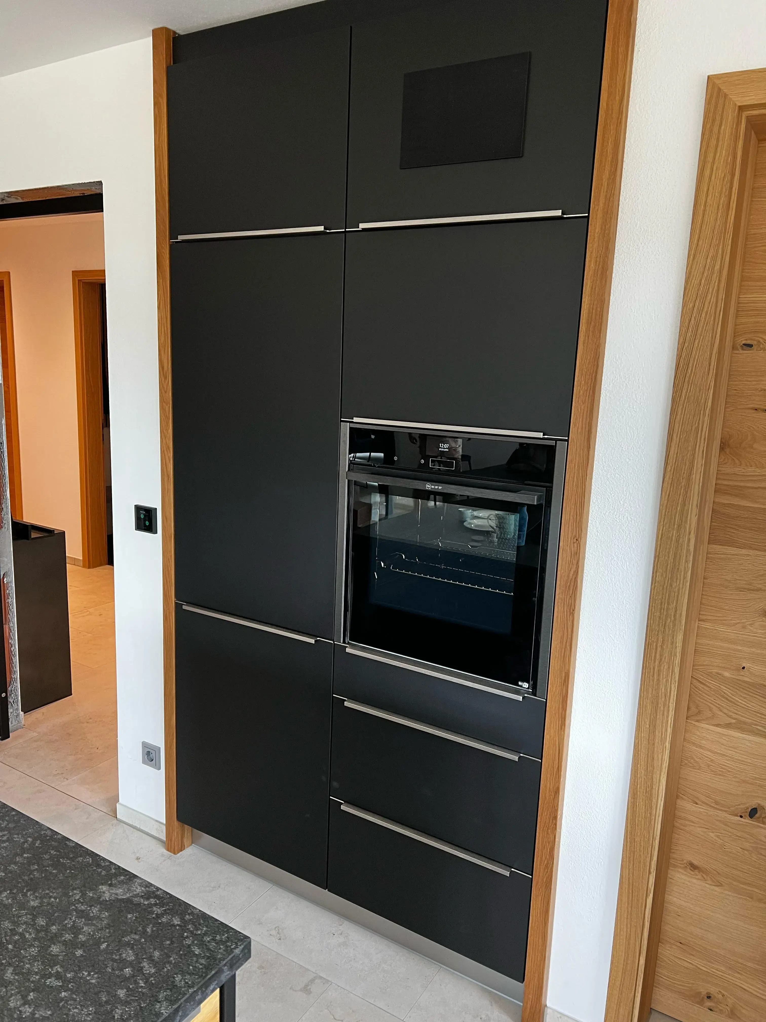 Moderne schwarze Küchenschränke mit integriertem Backofen und Holzrahmen.