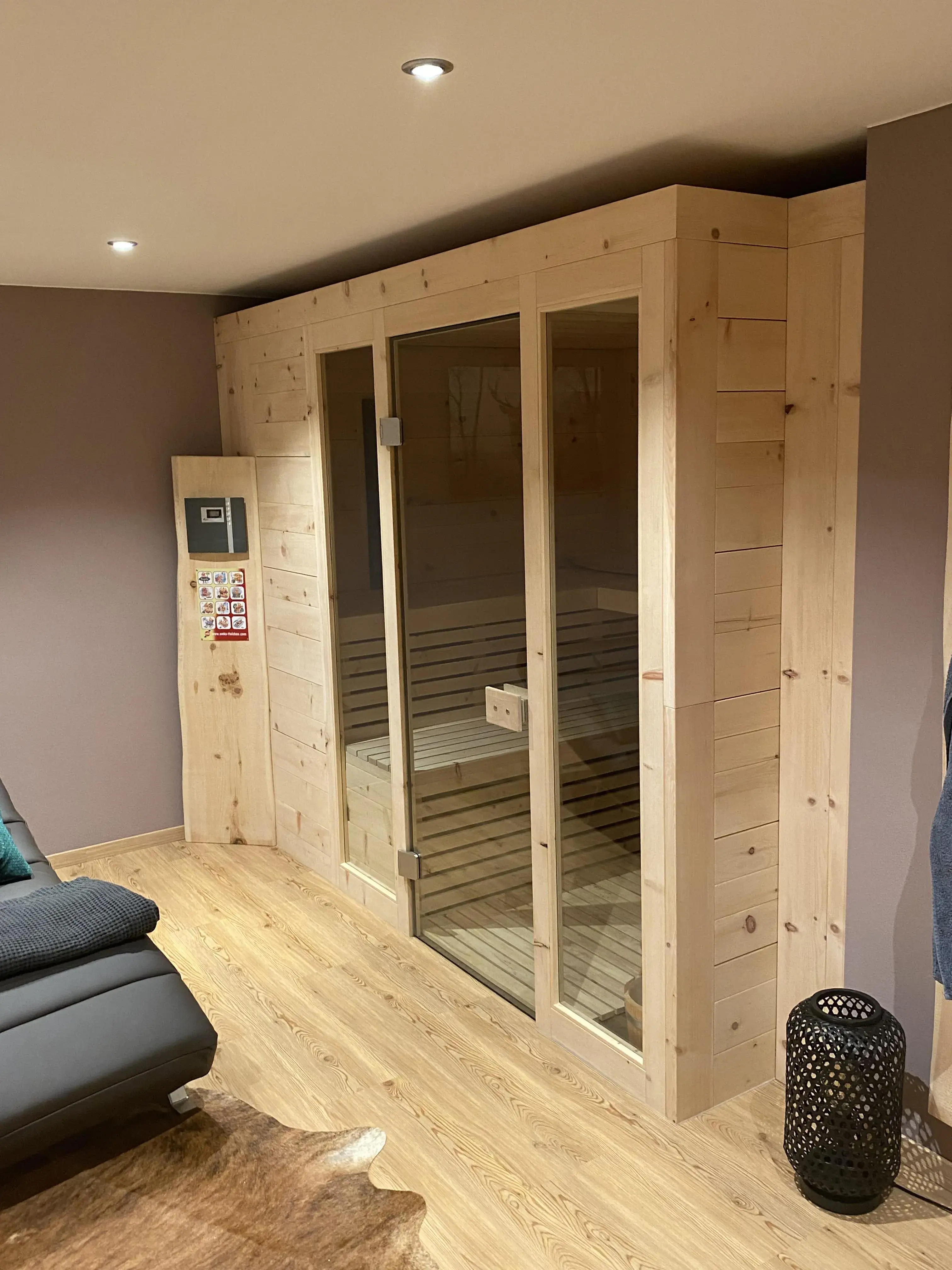Holzsauna mit Glastüren in modernem Wohnzimmer mit Holzboden und dezenten Farben.