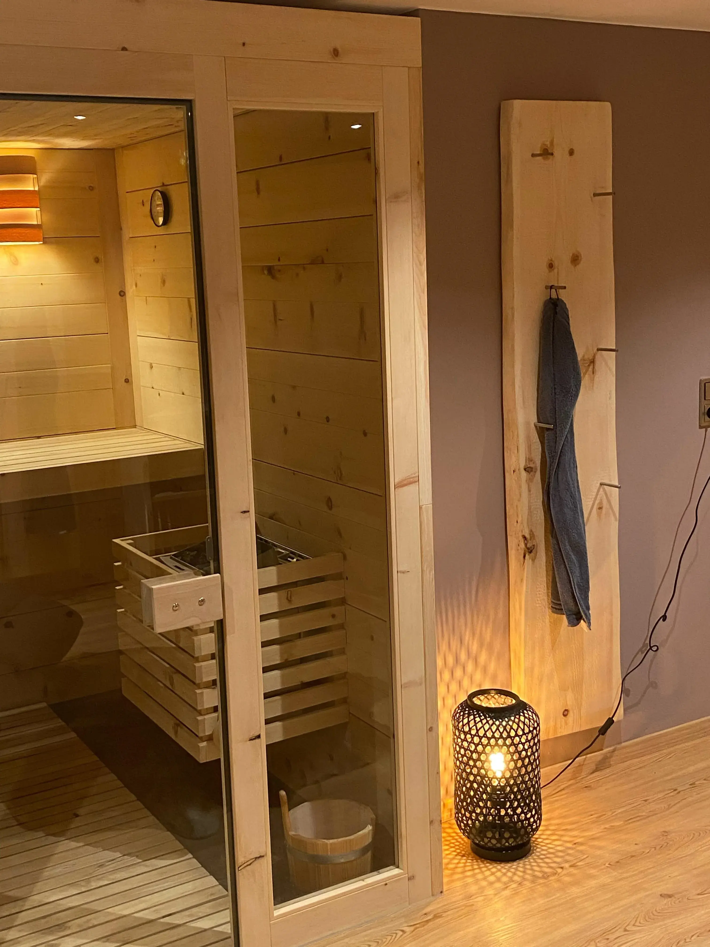 Sauna aus Holz, daneben eine Lampe und ein Handtuch an der Wand.