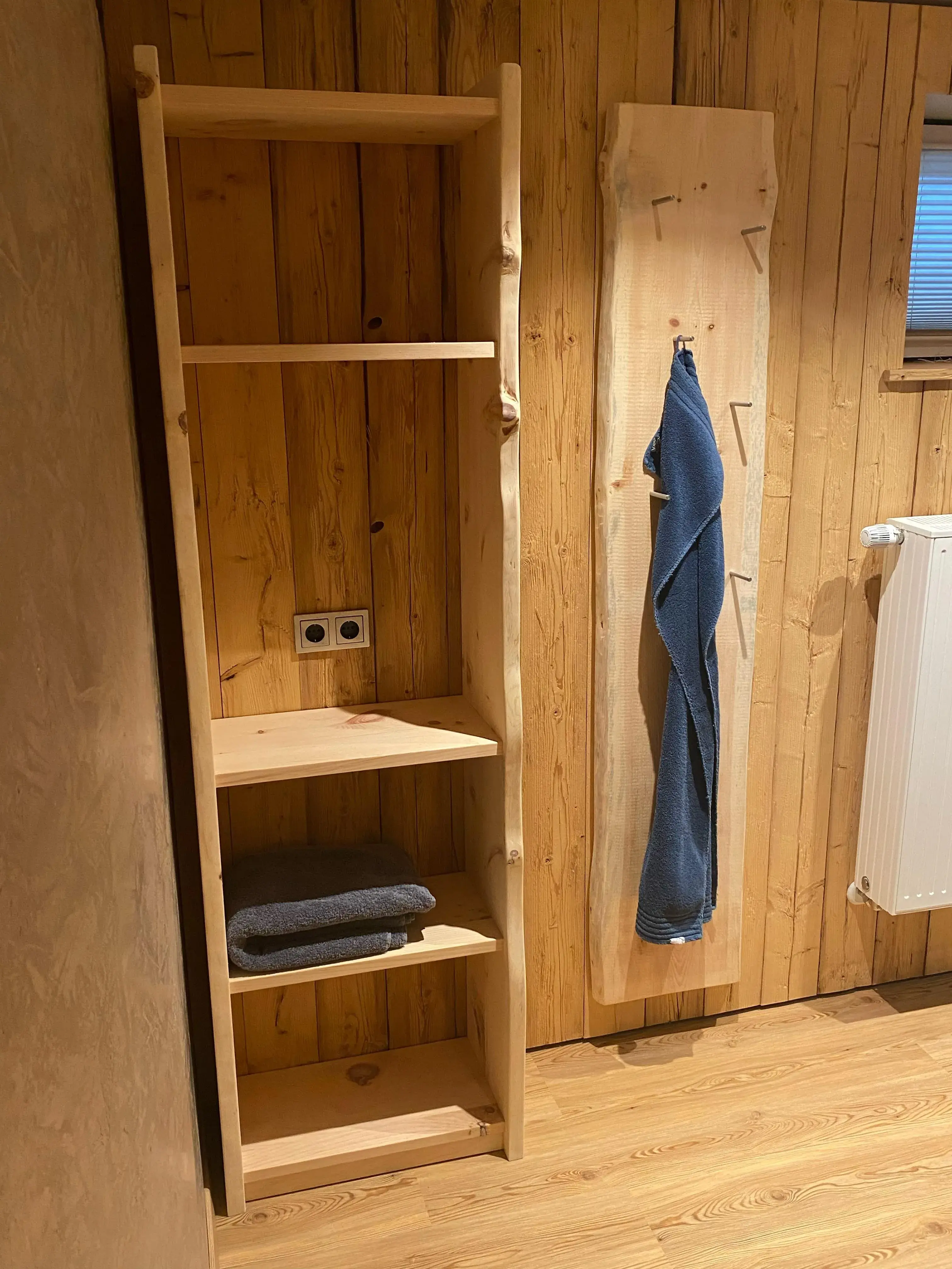 Offenes Holzregal mit Handtüchern in einem Holzraum, daneben ein Handtuchhalter.