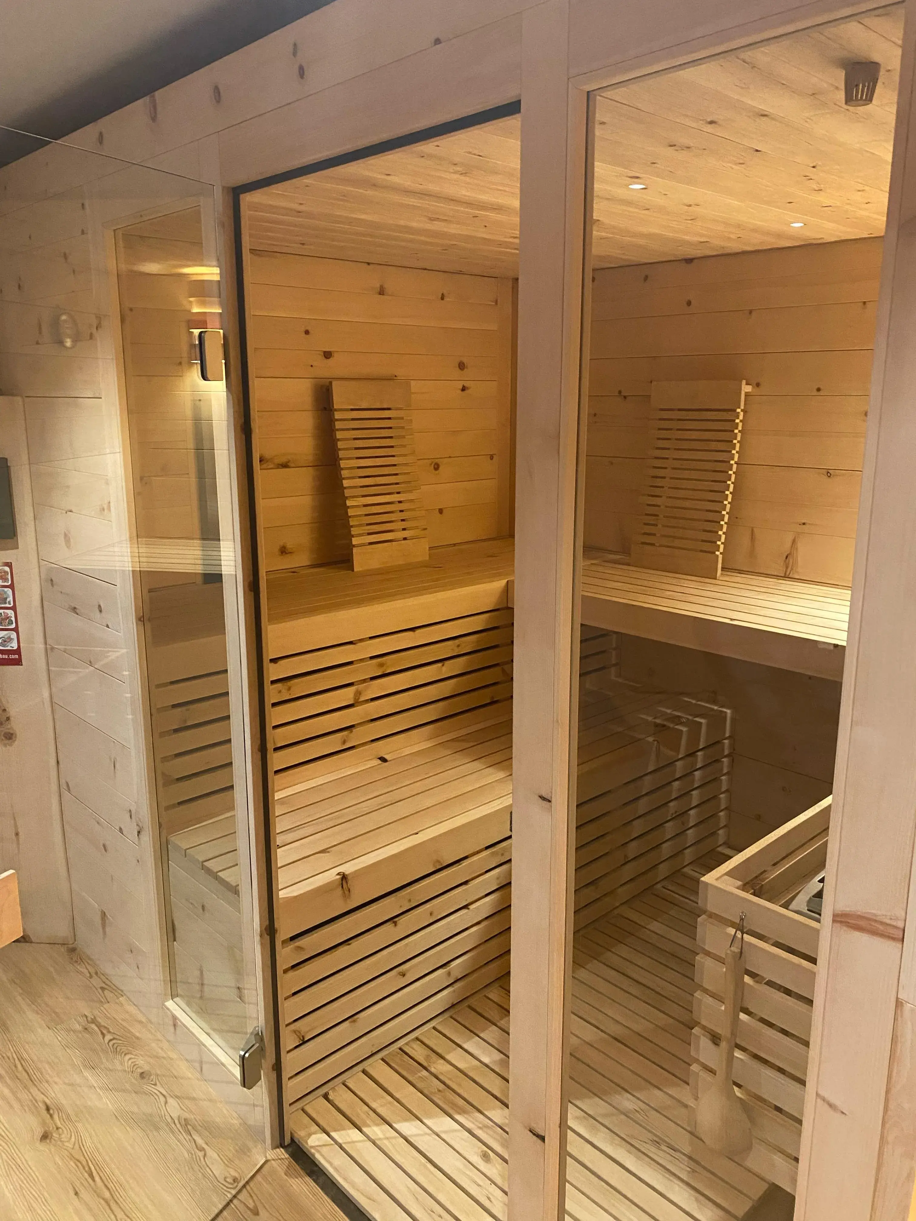 Holzsauna mit zwei Glaswänden und Holzbänken im Inneren.