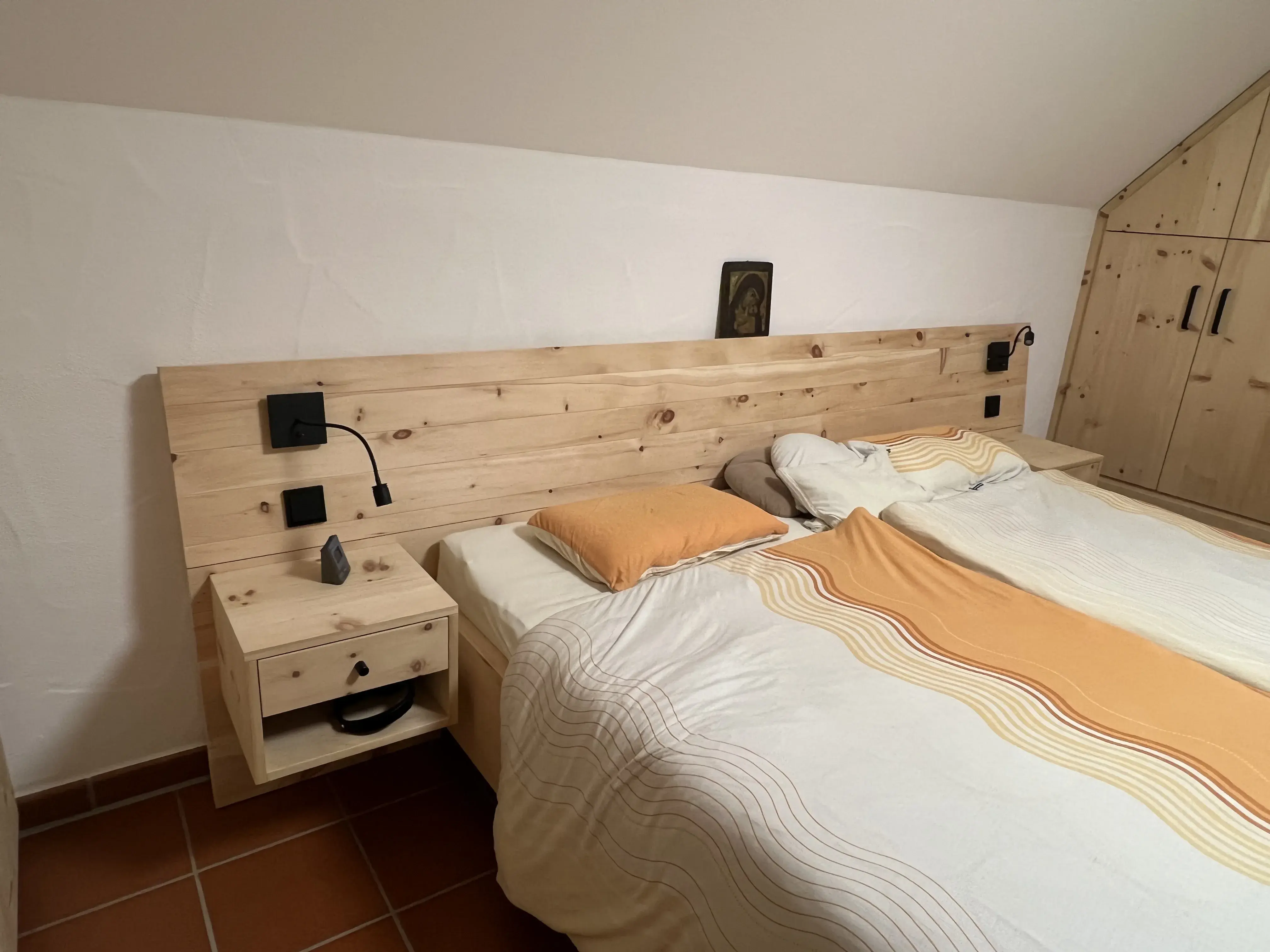Doppelbett mit Holz-Kopfteil, gelber Decke und Nachttisch in einem hellen Schlafzimmer.