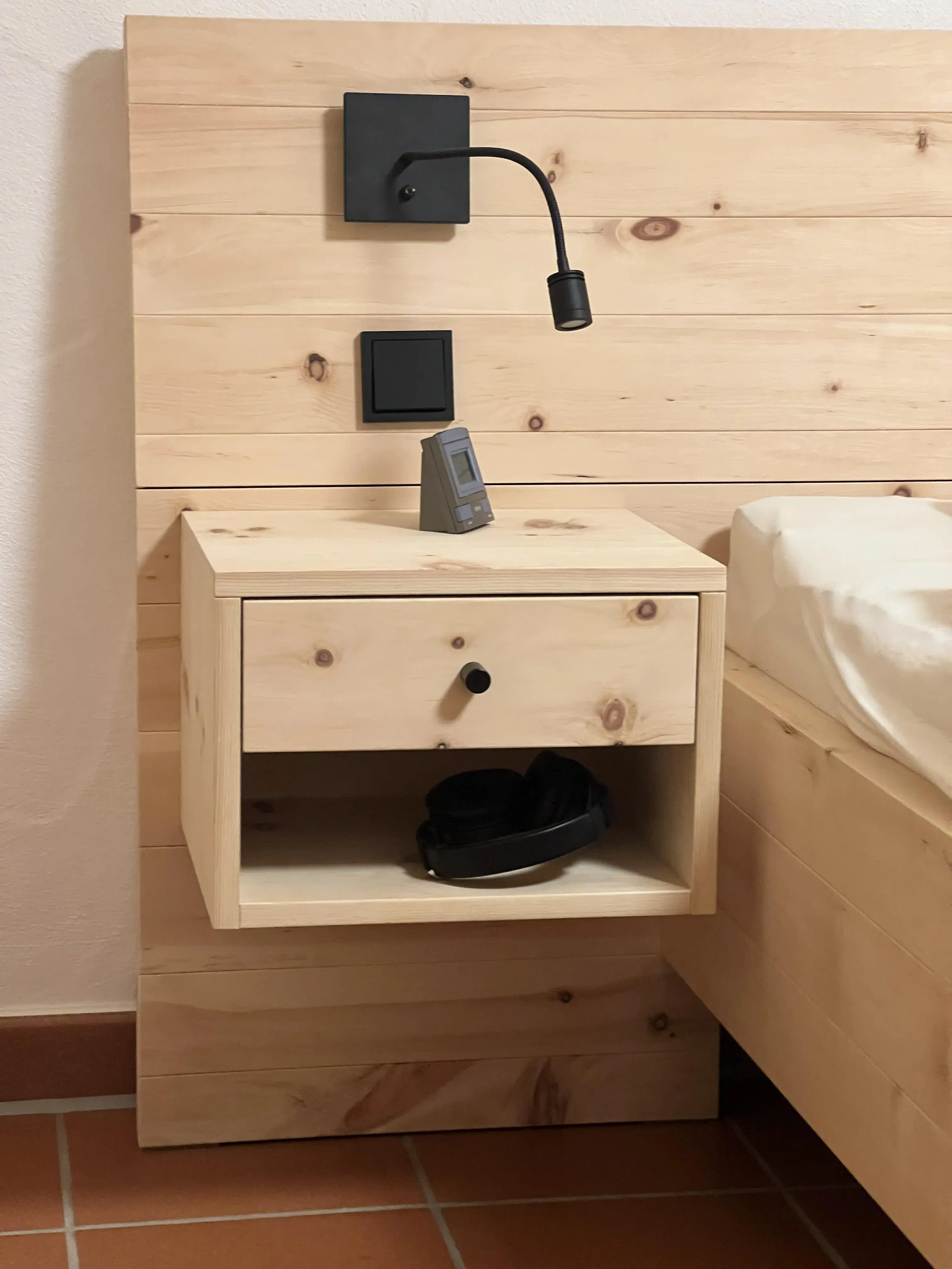 Heller Nachttisch aus Holz mit Lampe, Steckdose, Kopfhörern und kleinem Gerät