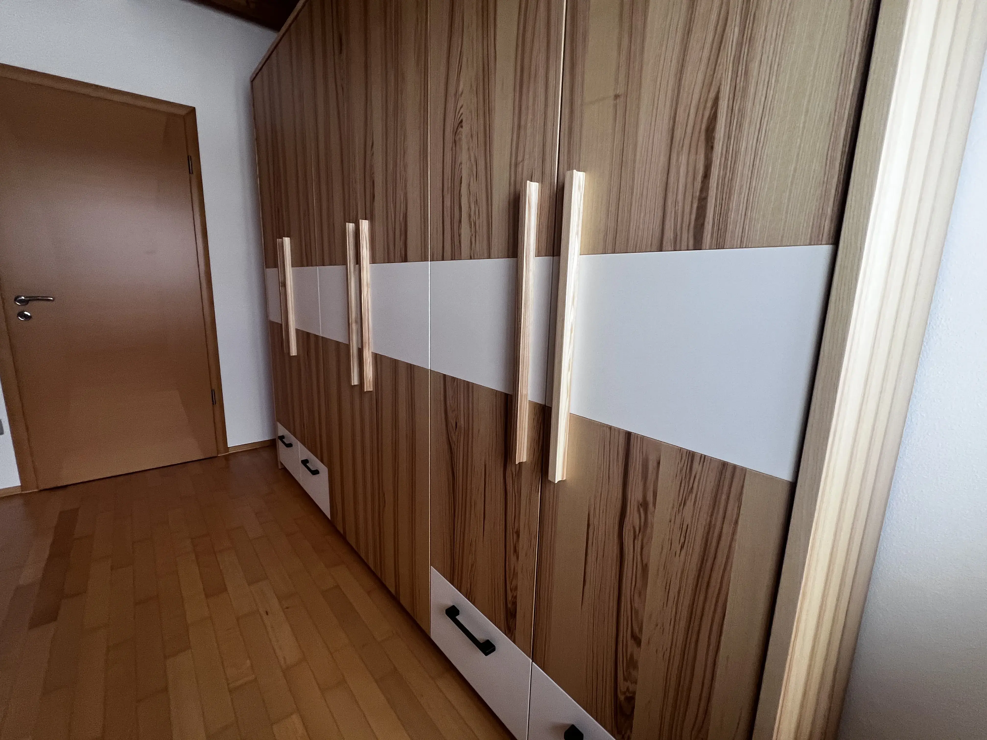 Großer Holzkleiderschrank mit weißen Streifen und langen Griffen in einem Zimmer.