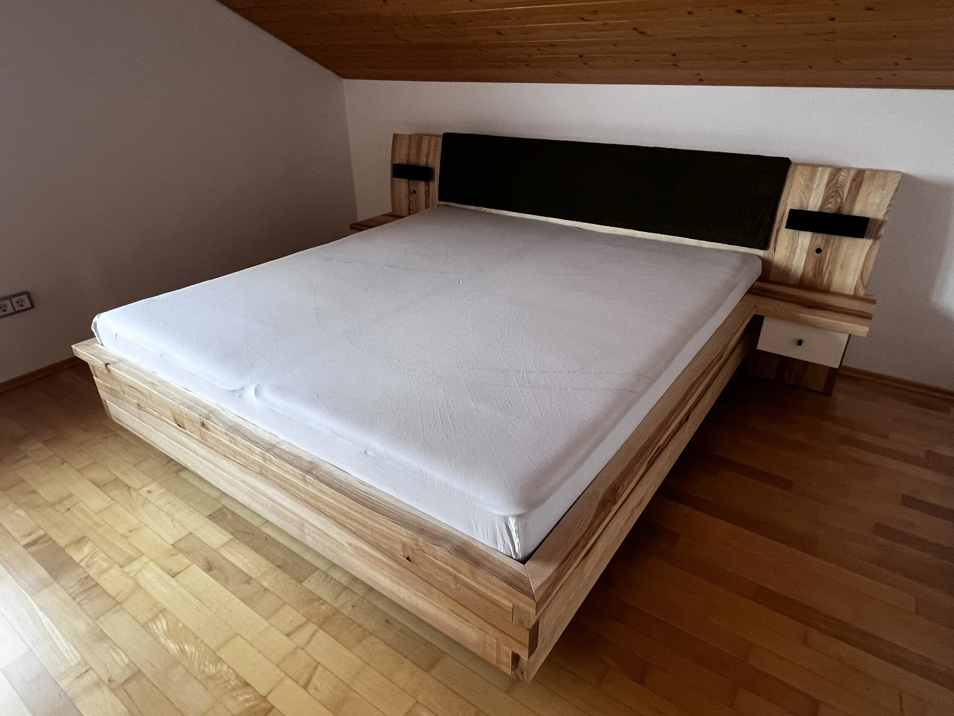 Doppelbett aus Holz mit weißer Matratze in einem Schlafzimmer mit Holzfußboden.