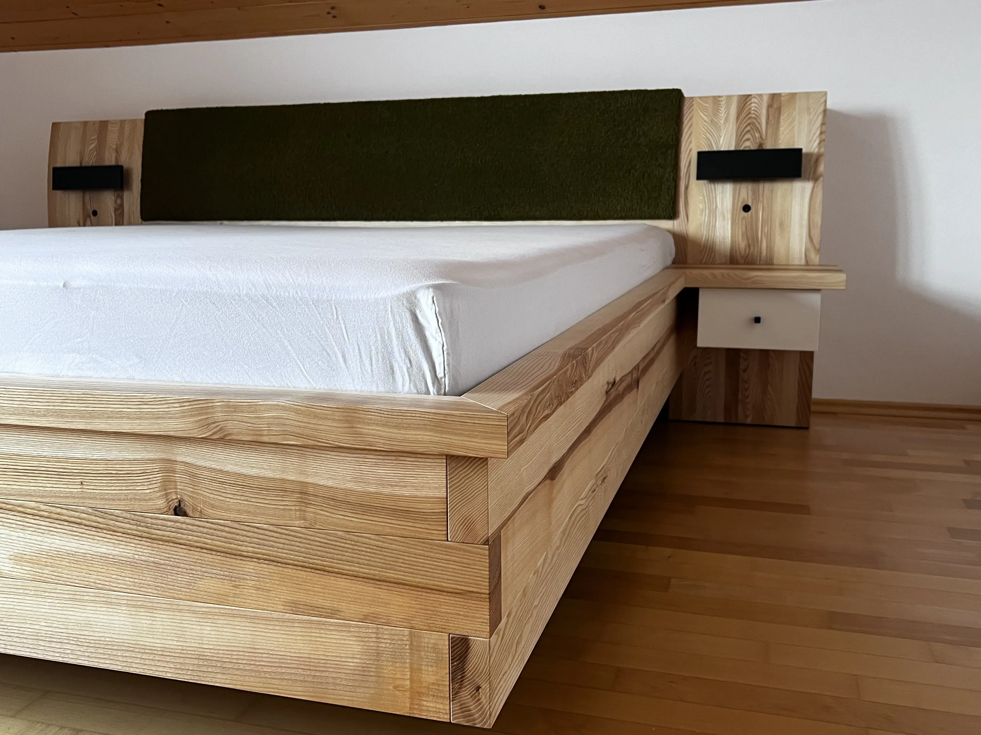 Holzbett mit weißer Matratze und grünem Polsterkopfteil auf Holzfußboden.
