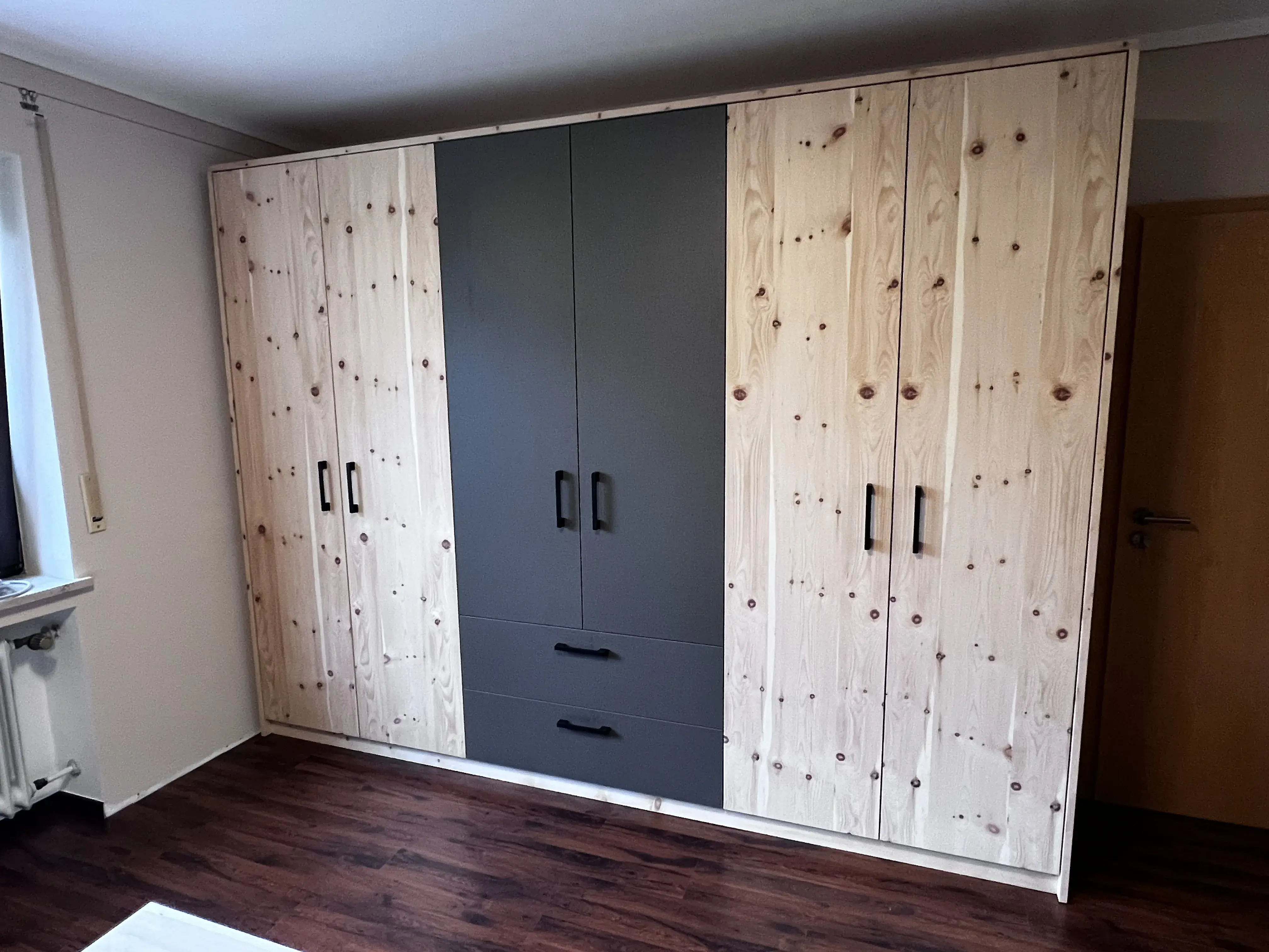 Großer Kleiderschrank aus Holz mit mittleren grauen Türen in einem Zimmer mit dunklem Boden.